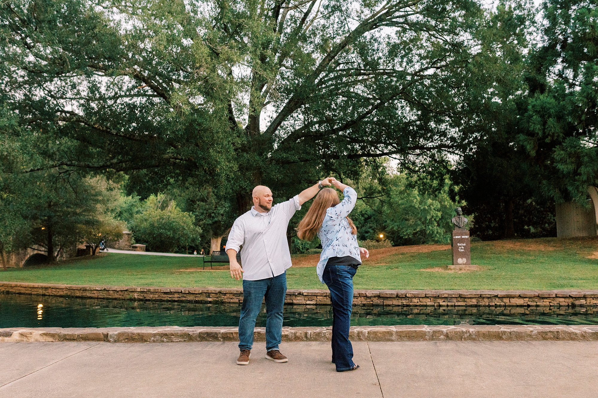 man twirls woman inside Charlotte NC park during NC engagement photos