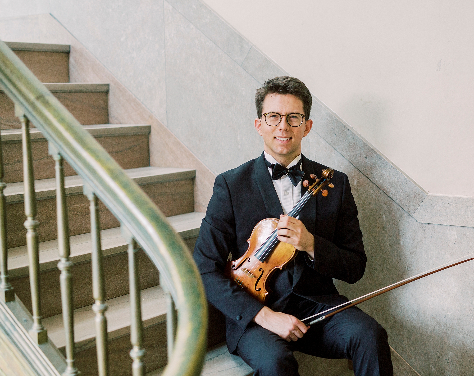 violin player sits on steps holding violin under his arm