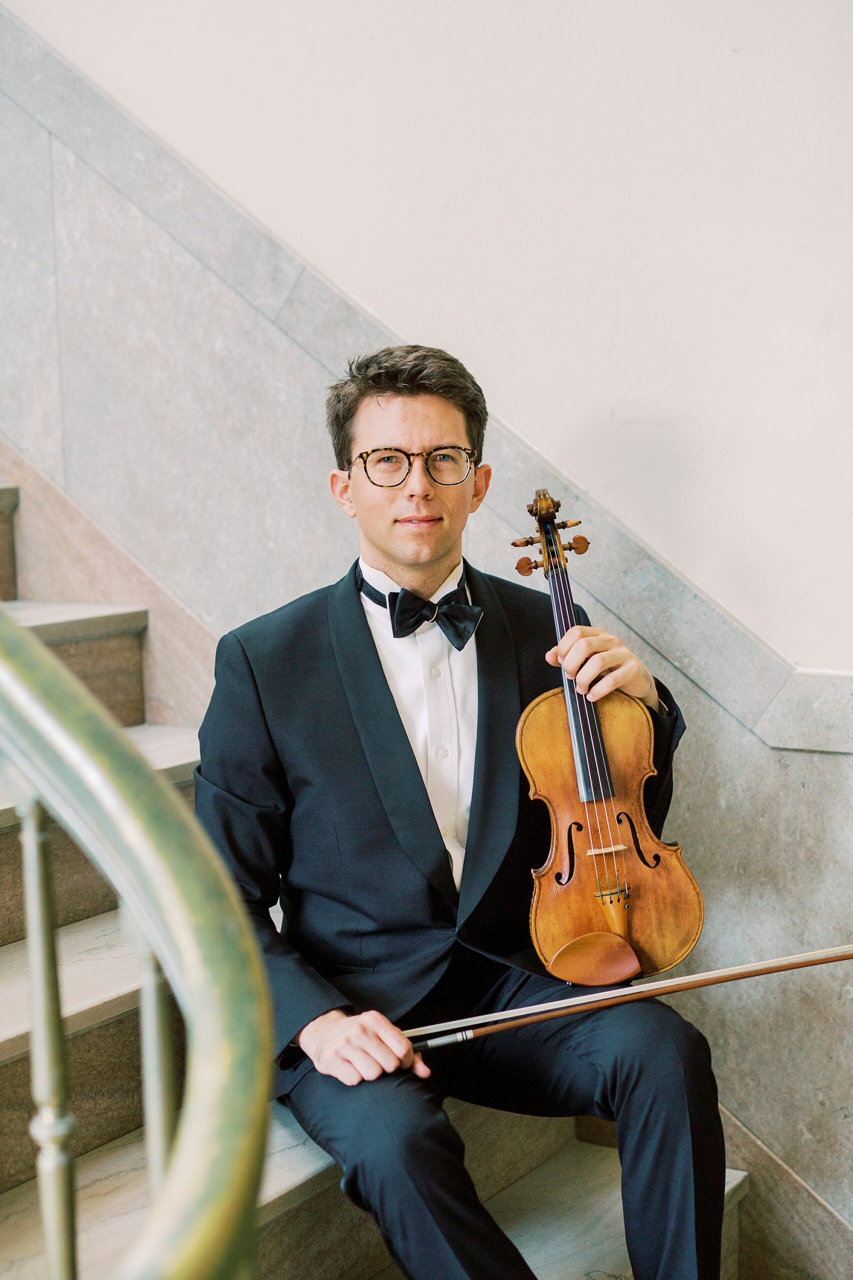 man sits on stairs holding violin during headshots 