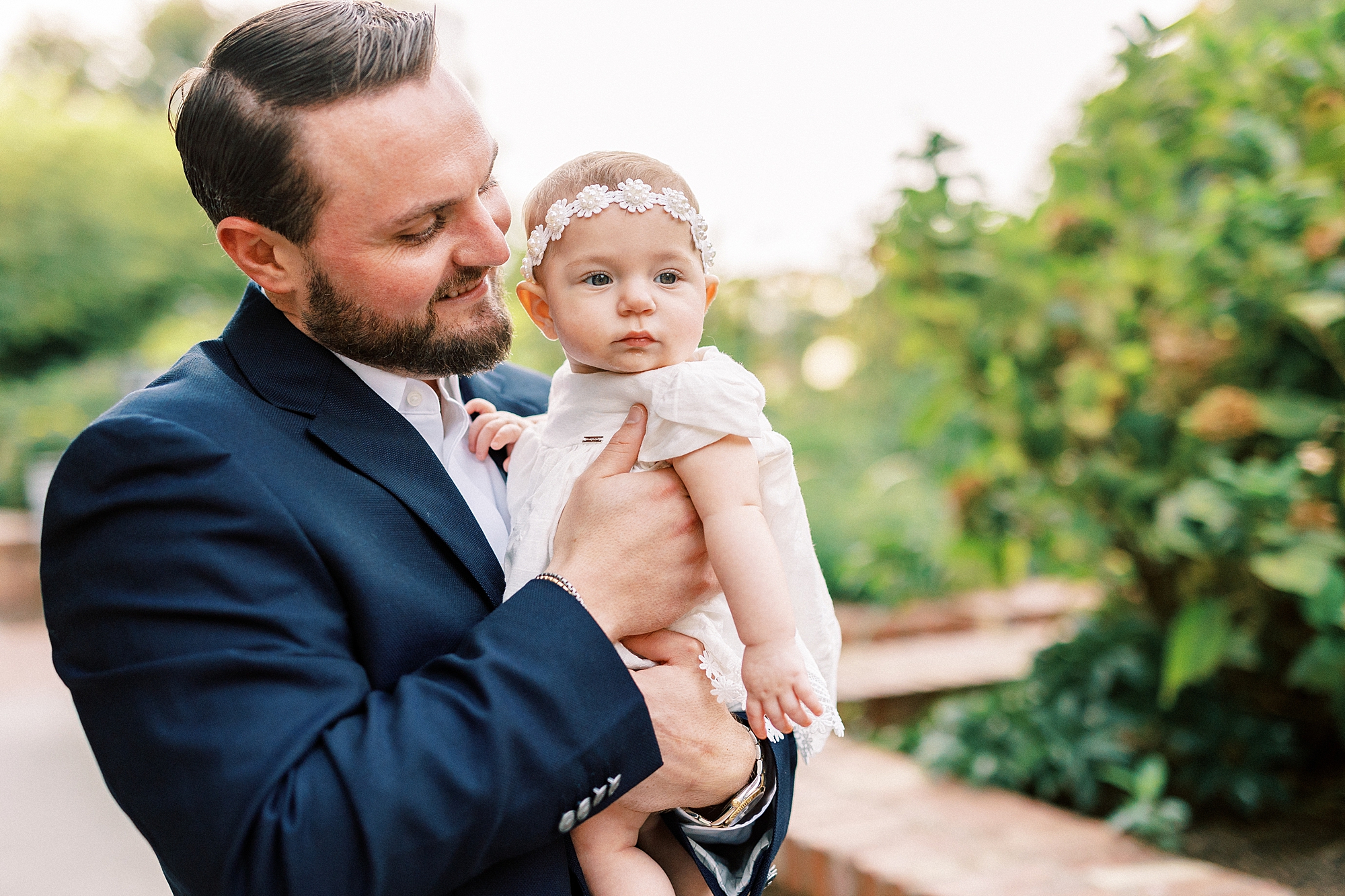man in navy suit holds daughter on hip during engagement photos in Romare Bearden Park