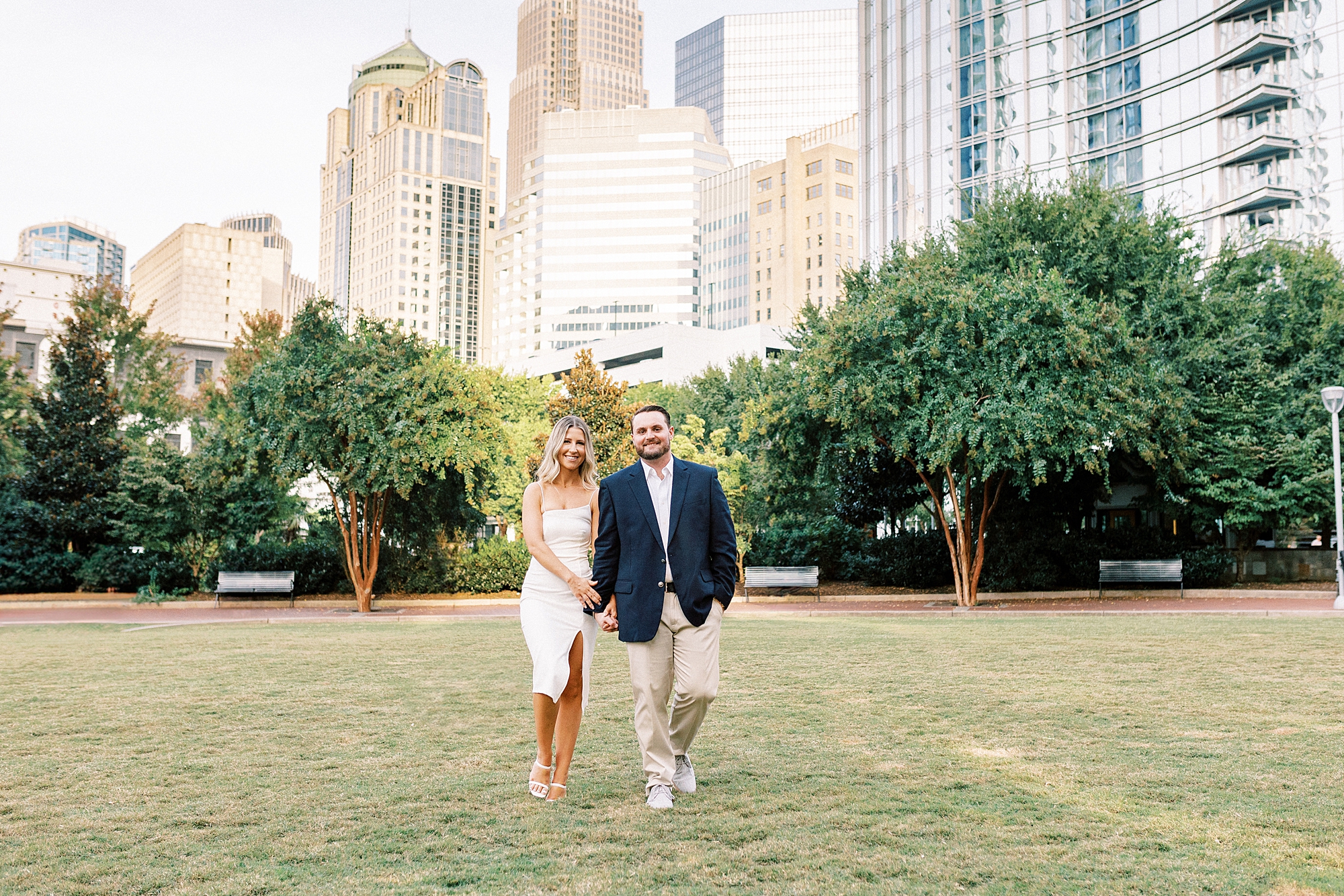 couple holds hands walking through Romare Bearden Park during engagement portraits 