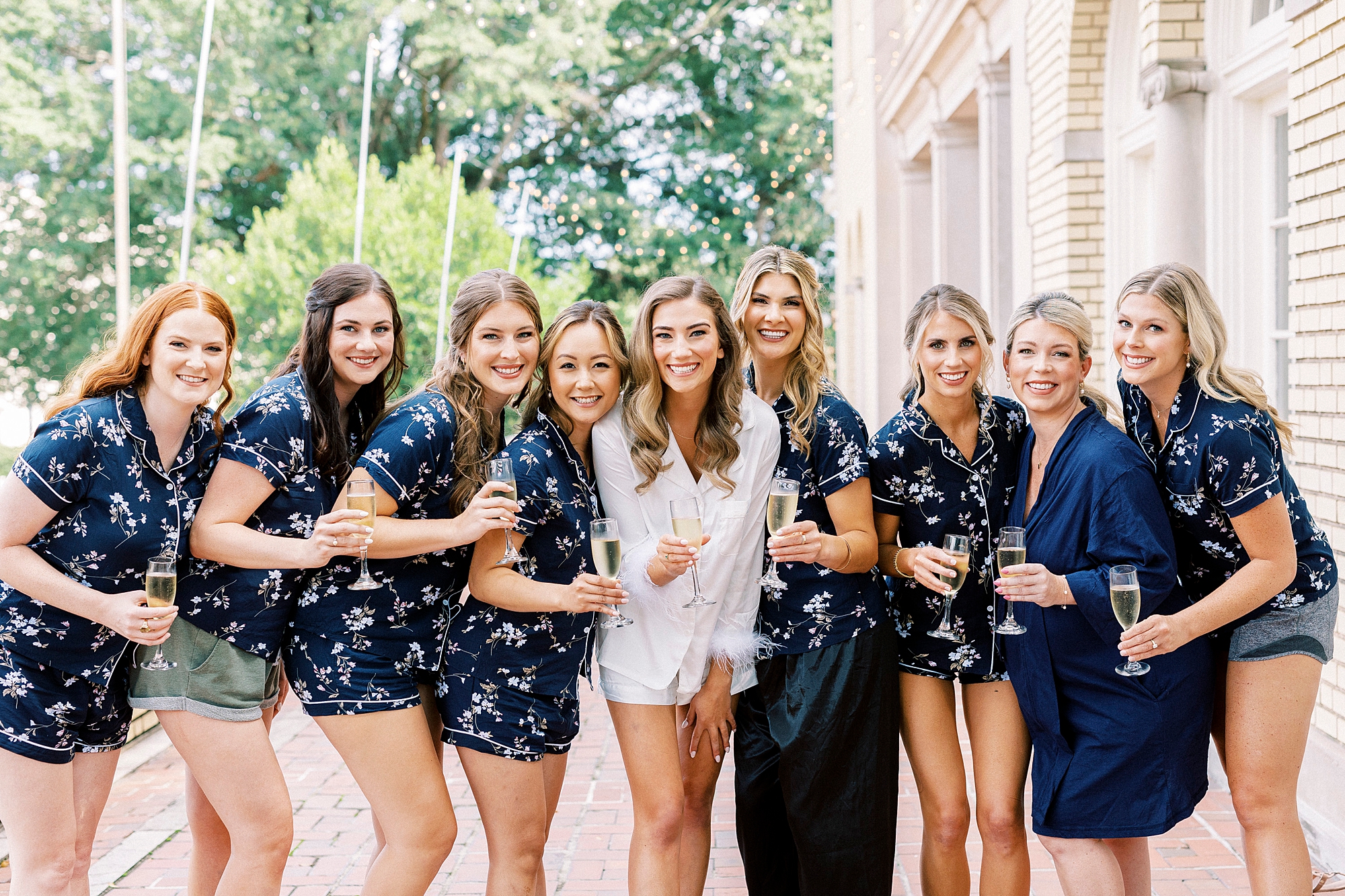 bride smiles with bridesmaids in navy pajamas outside Separk Mansion with champagne glasses 