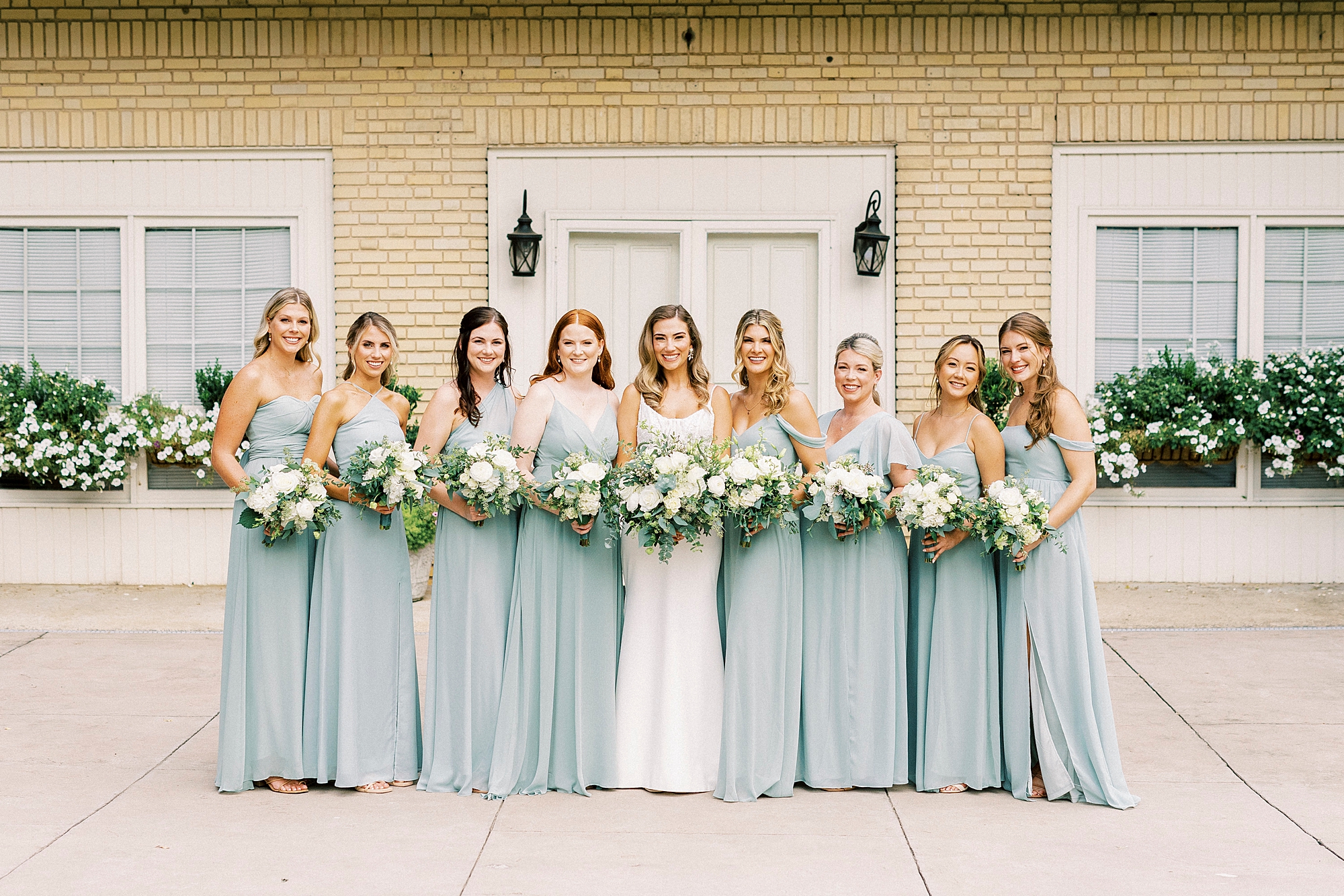 bride poses with bridesmaids in blue gowns with ivory rose and flower bouquet 