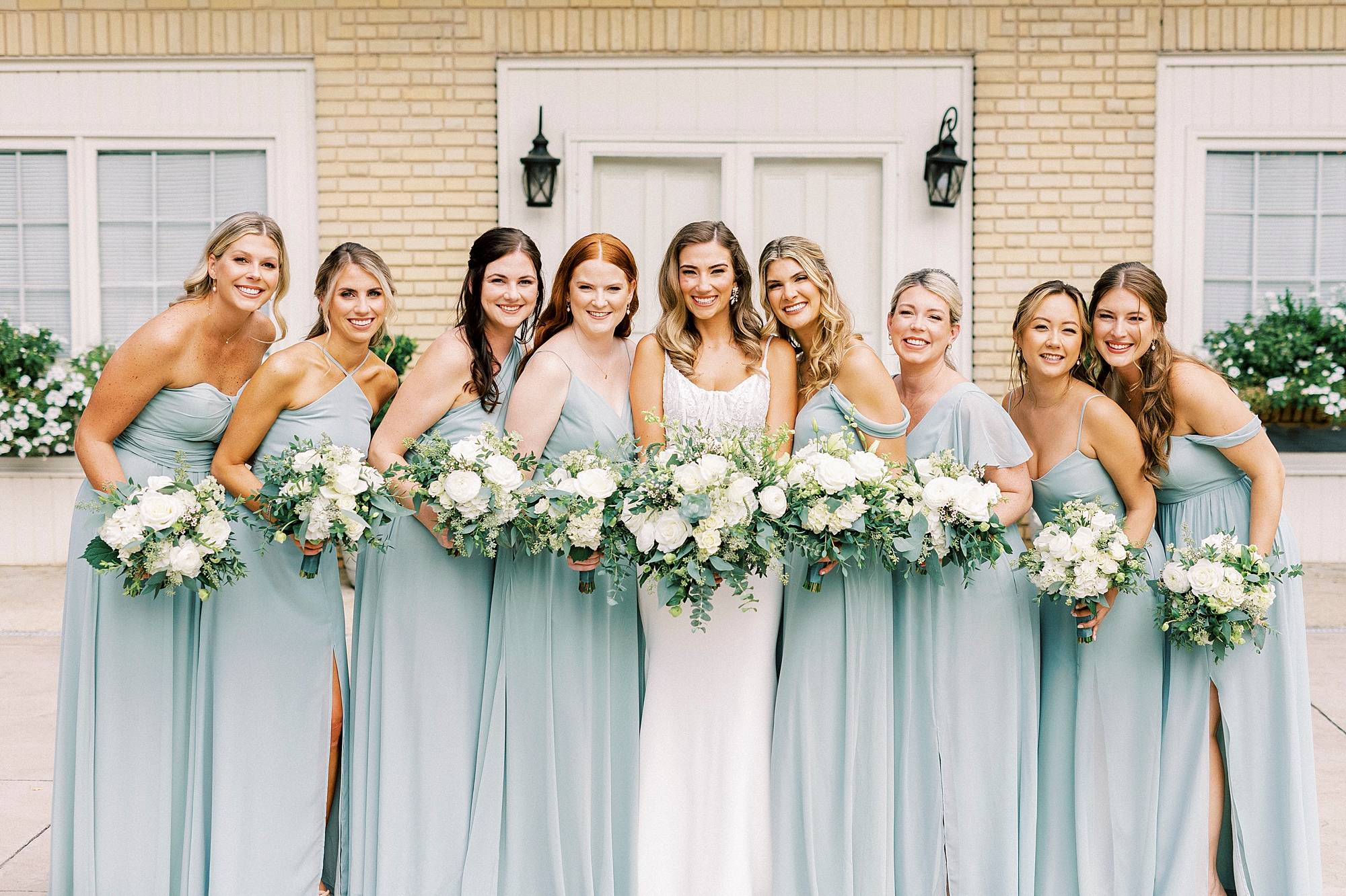 bride and bridesmaids hug together outside Separk Mansion holding bouquet of ivory flowers