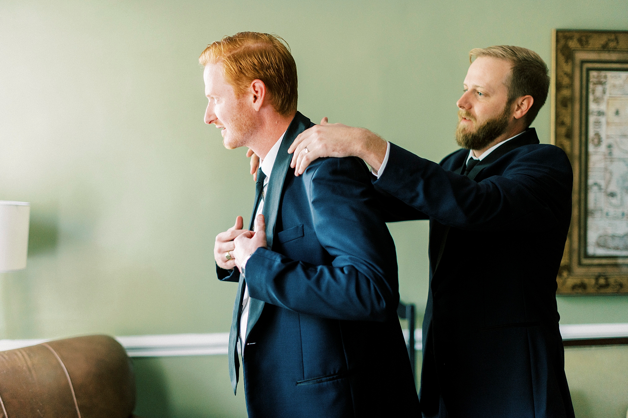 groomsman helps groom into navy suit jacket at Separk Mansion