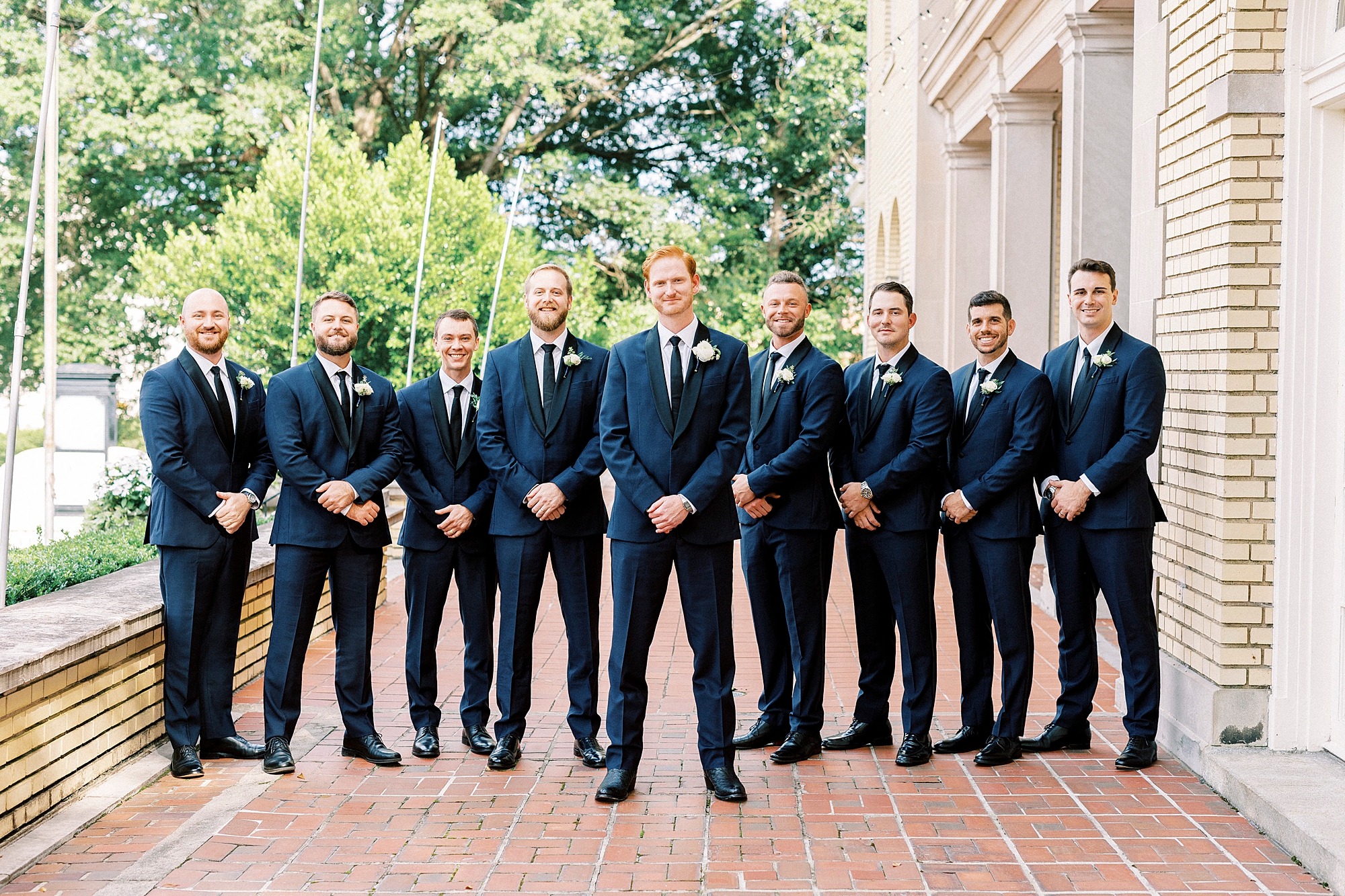 groom stands with groomsmen in navy suits on brick patio outside Separk Mansion