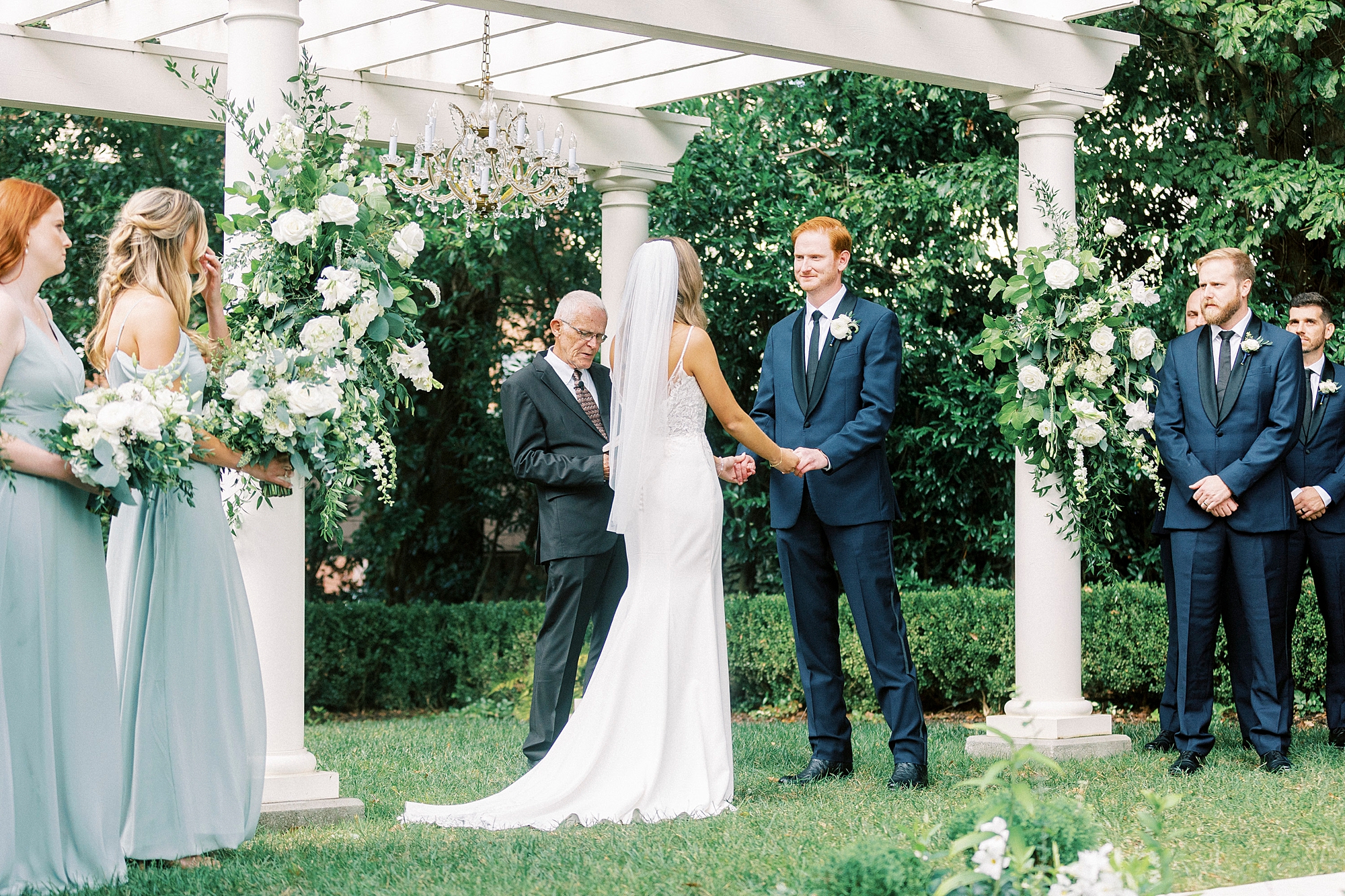 newlyweds hold hands under white pergola for outdoor wedding ceremony at Separk Mansion
