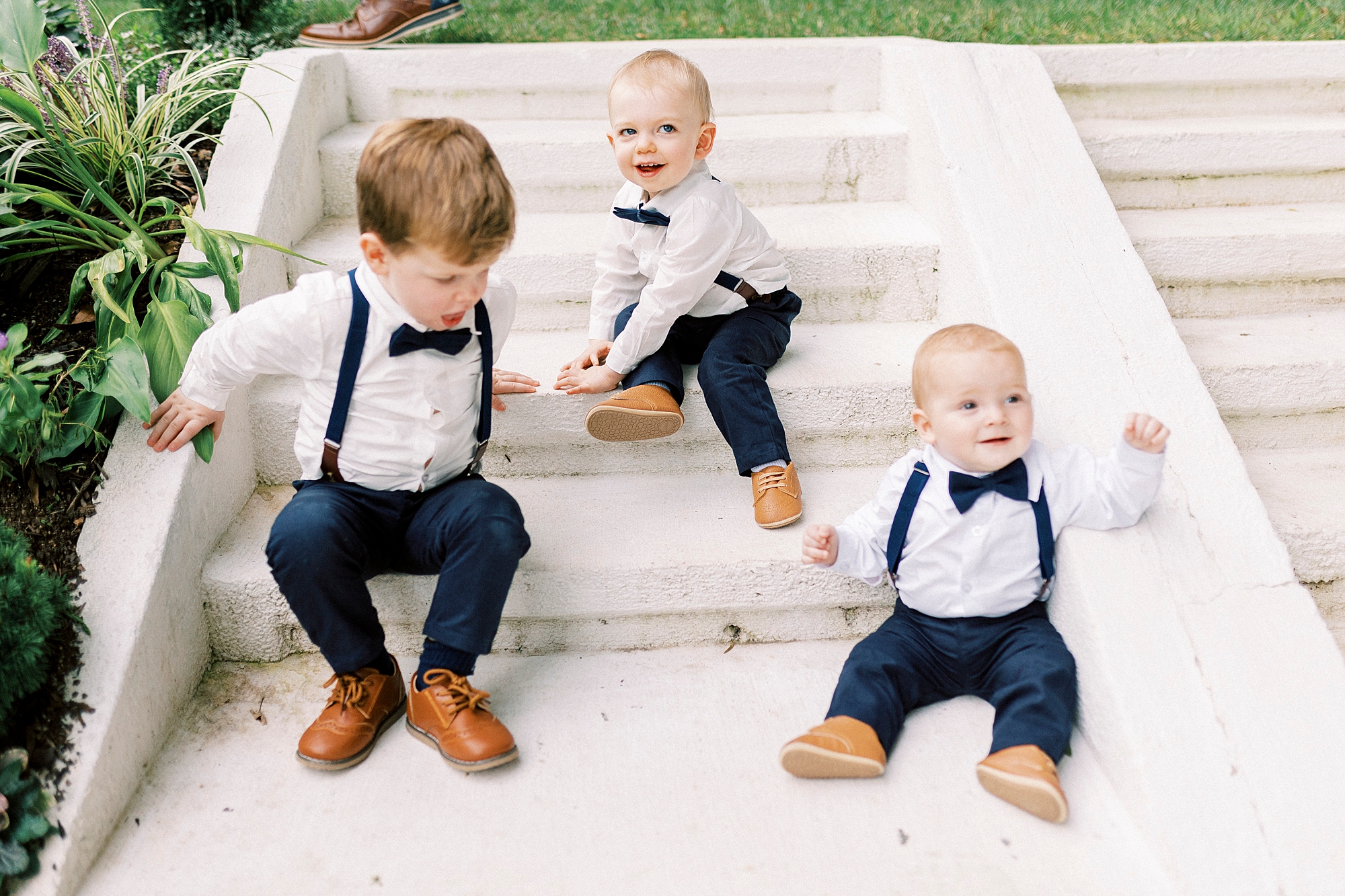 ring bearers sit in navy suspenders and bow ties on steps at Separk Mansion
