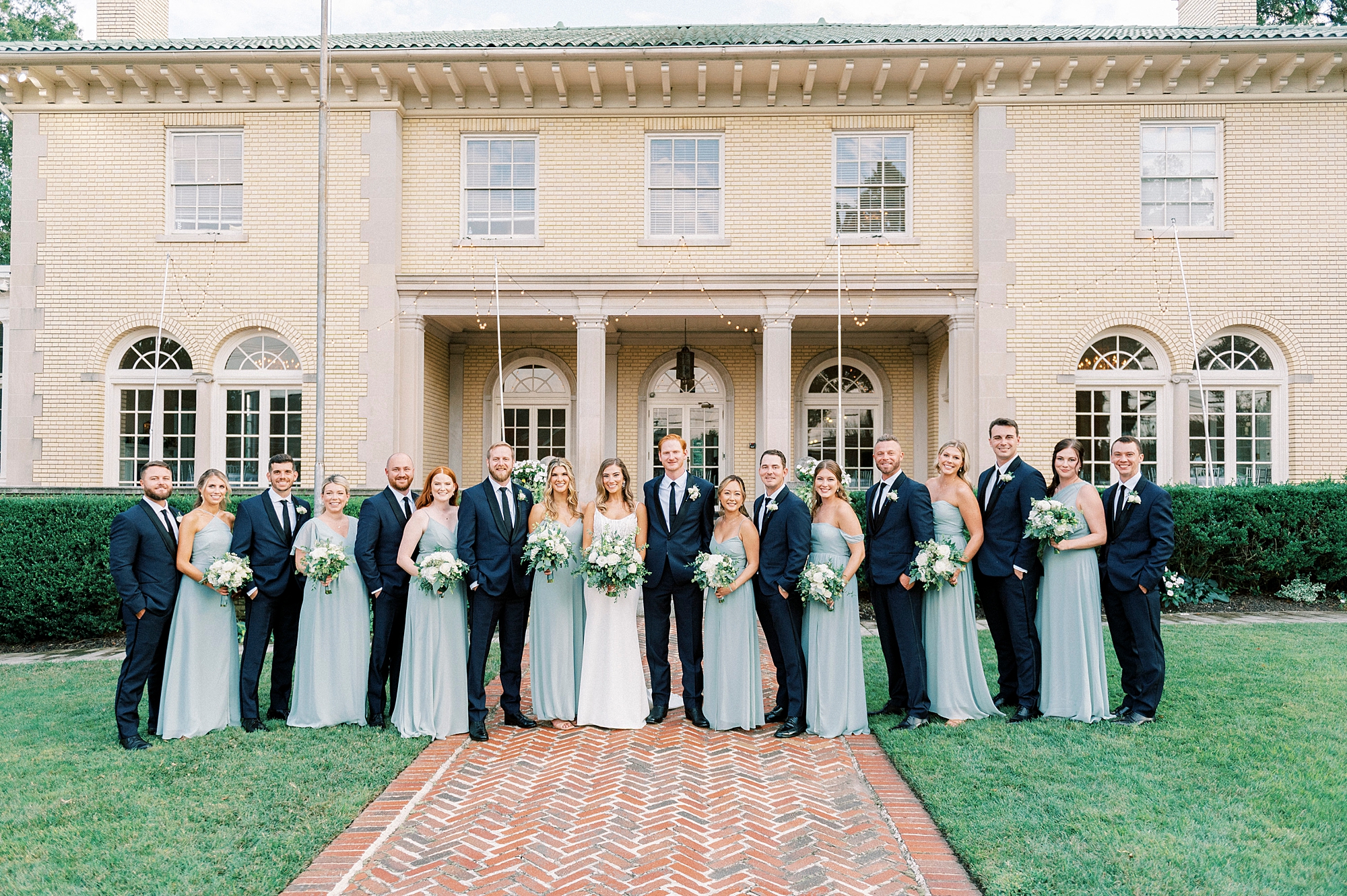 bride and groom stand with wedding party in light blue gowns and navy suits