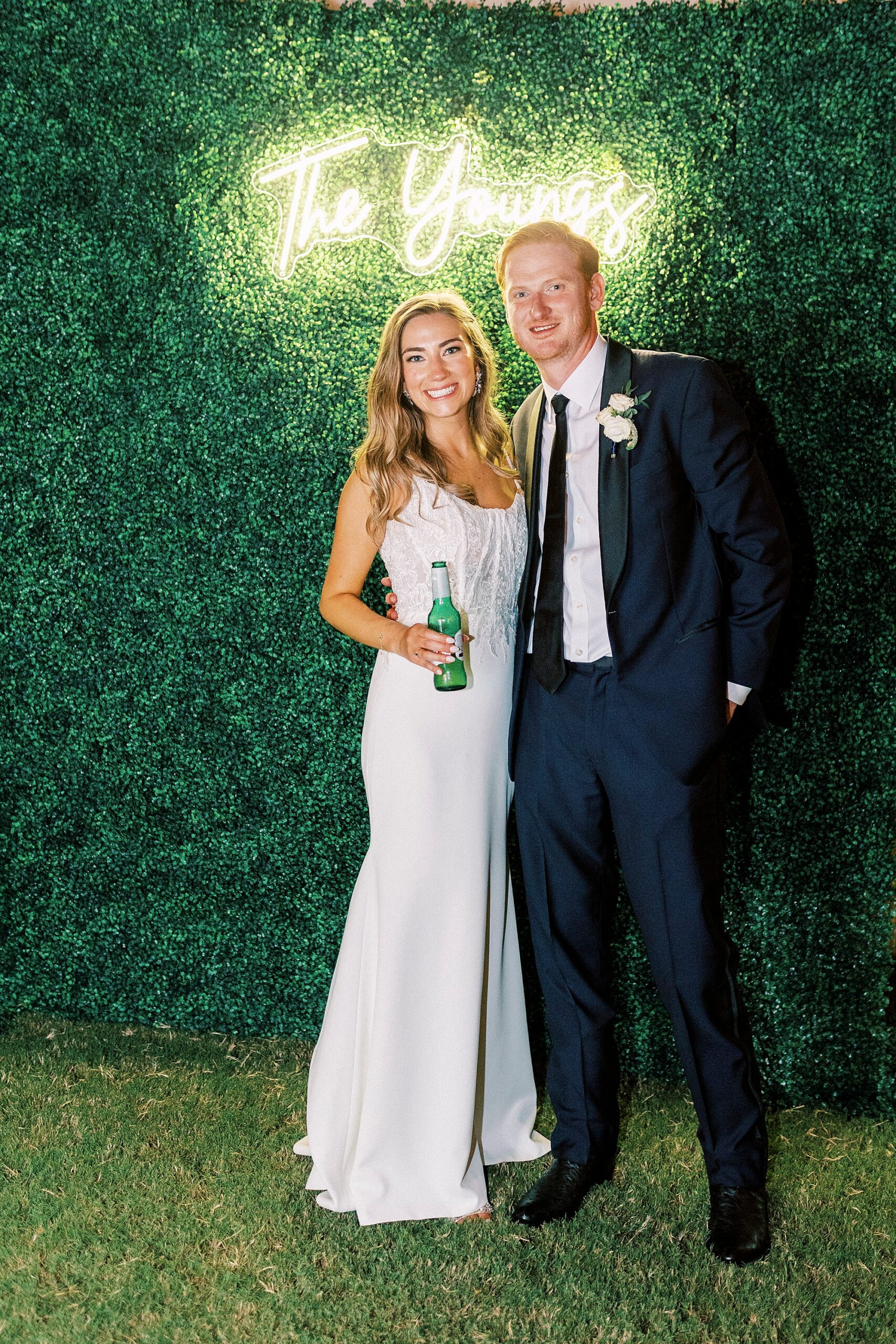 newlyweds hug in front of custom neon sign and greenery wall at NC wedding reception