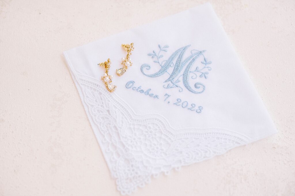 gold earrings lay on bride's handkerchief with blue lettering 