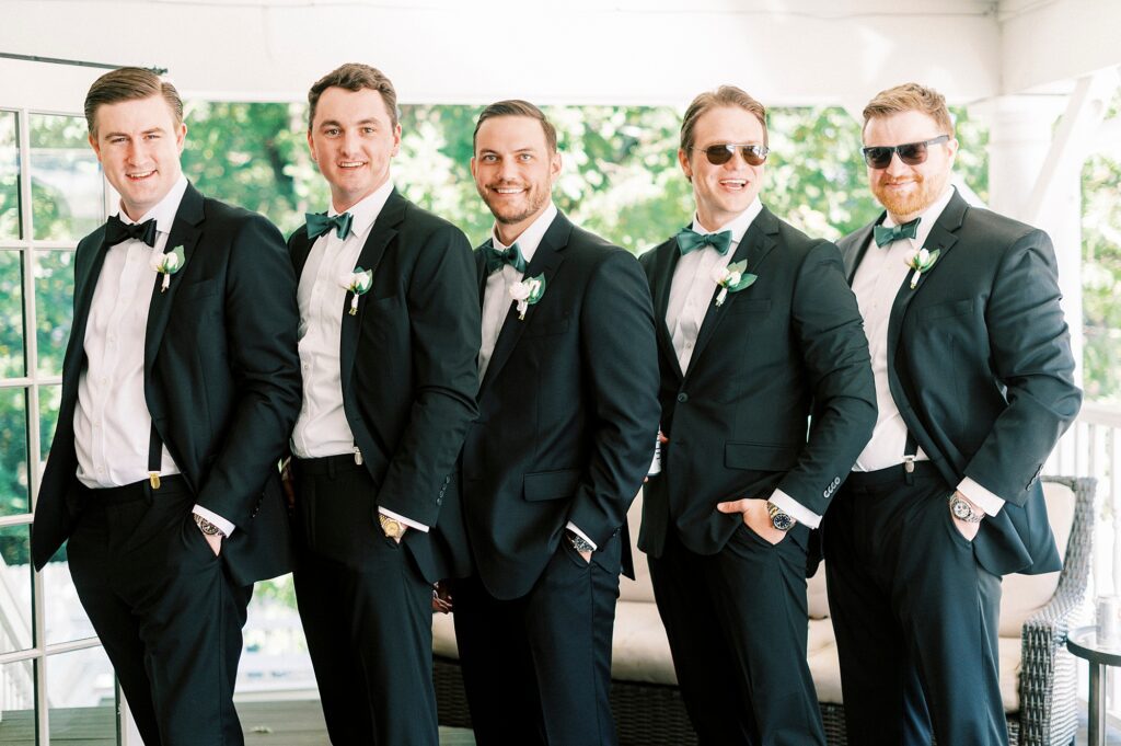 groom poses with groomsmen in black suits at Whitehead Manor