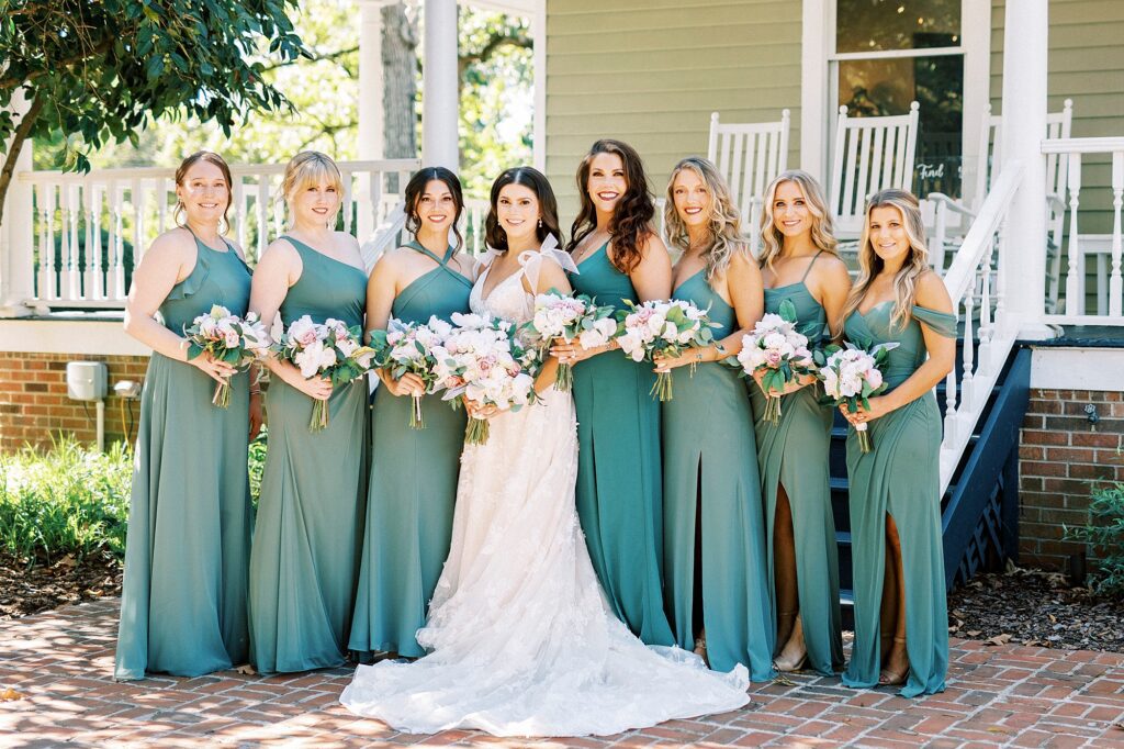 bride and bridesmaids in green gowns pose outside Whitehead Manor holding pastel bouquets 