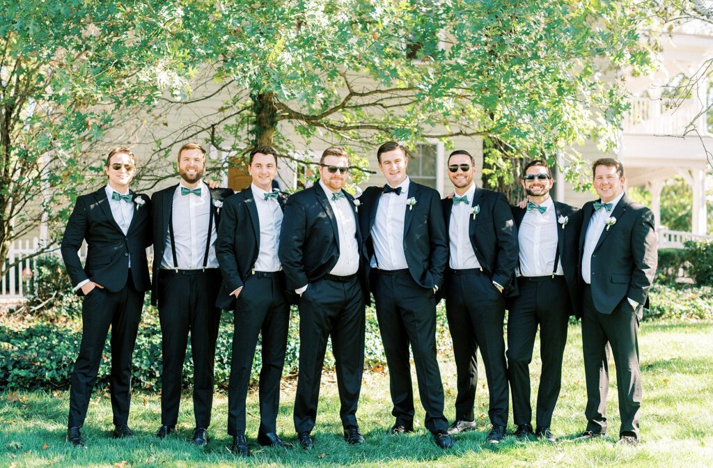 groom stands with groomsmen in black suits at Whitehead Manor