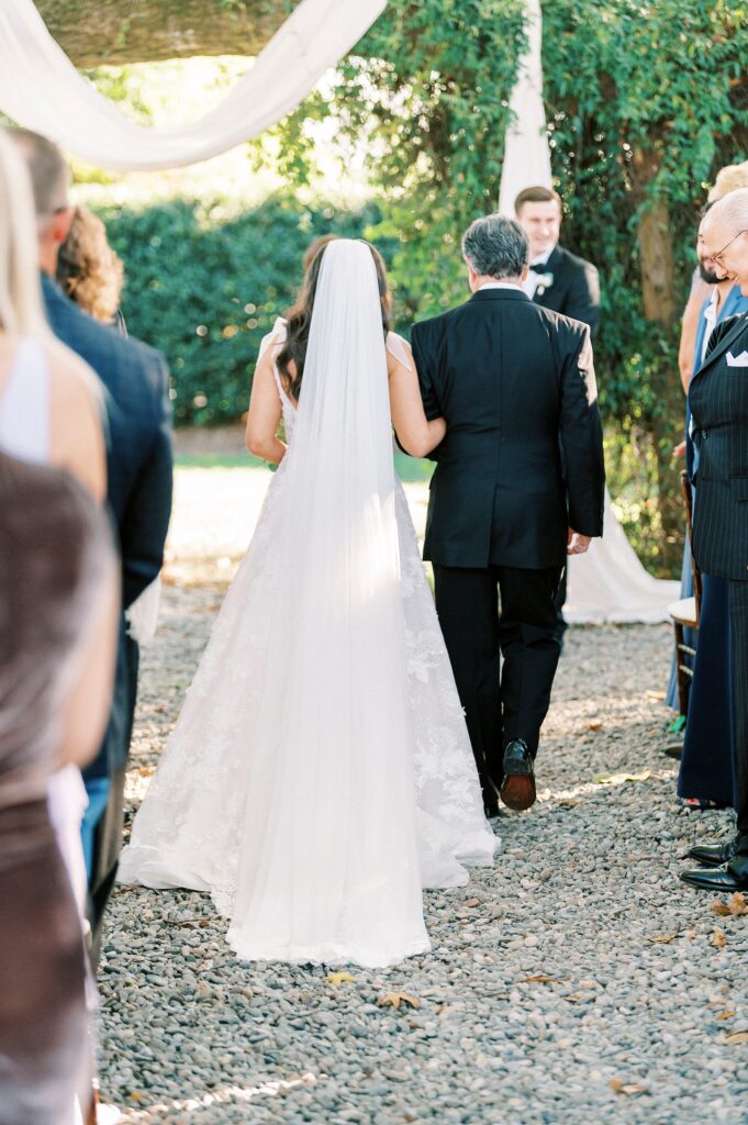 bride walks down aisle towards oak tree for ceremony at Whitehead Manor