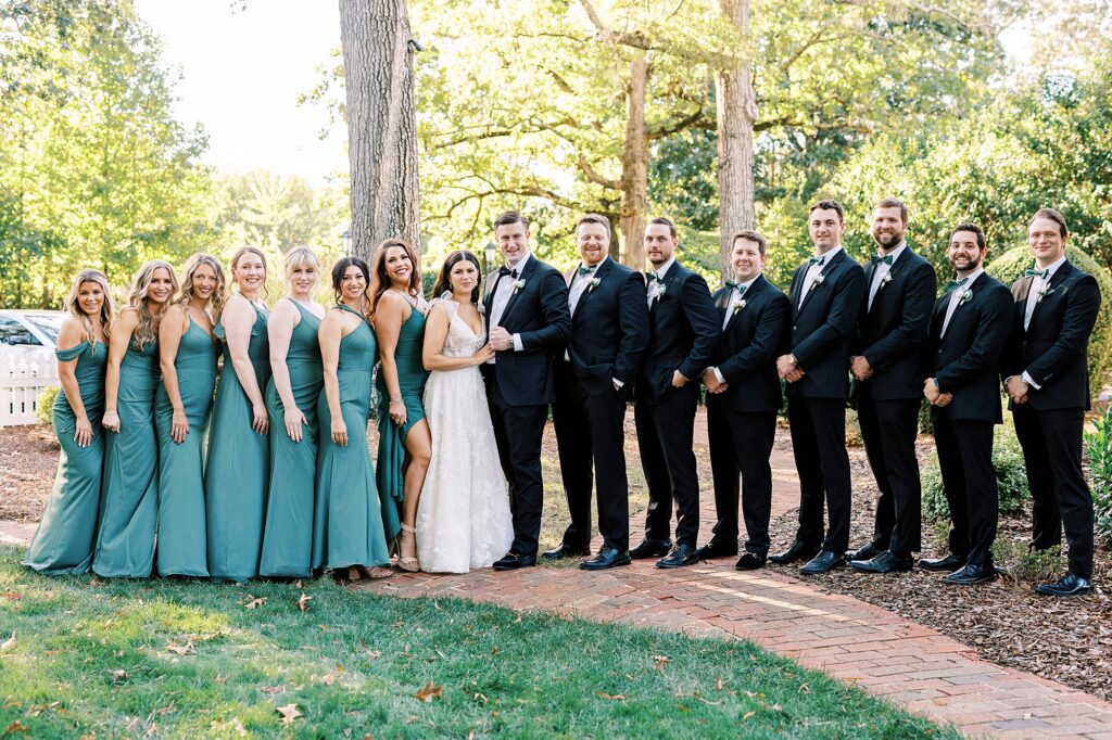 bride and groom pose with wedding party in green gowns and black suits 