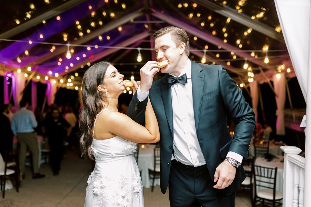 bride and groom link arms biting into donuts during Charlotte NC wedding reception 
