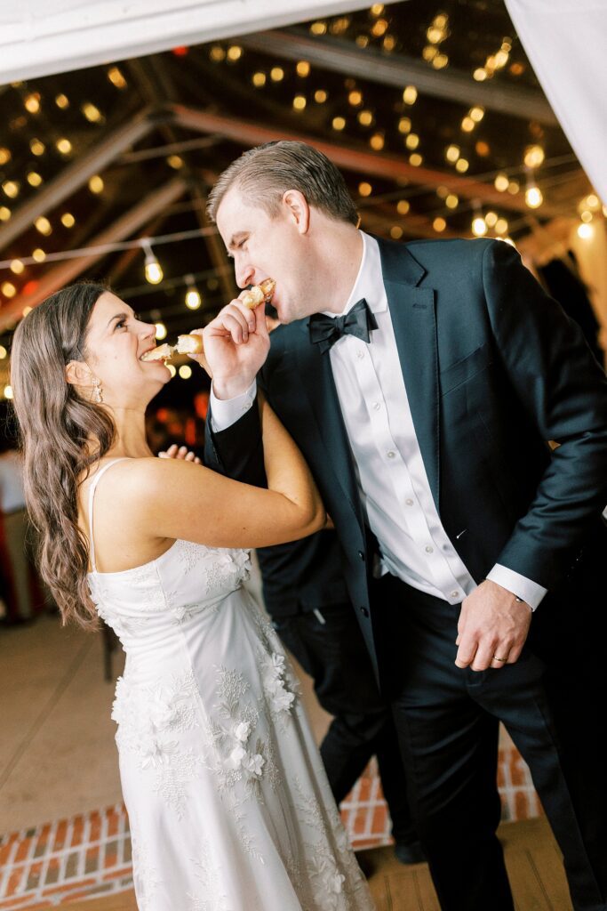 newlyweds eat donuts with linked arms during NC wedding reception 