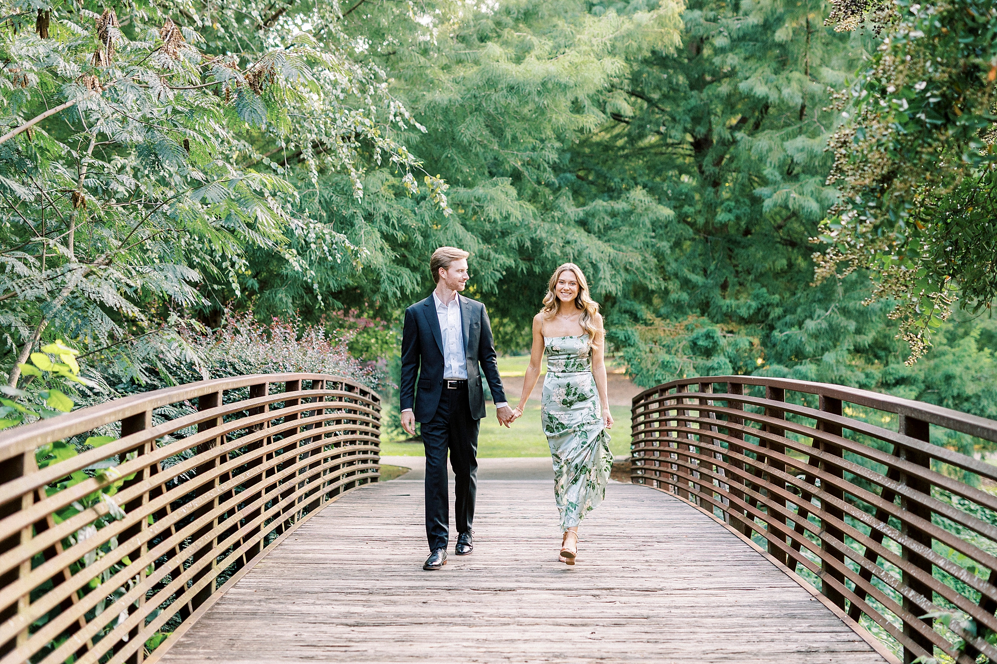 engaged couple holds hands walking on wooden bridge in Glencairn Garden