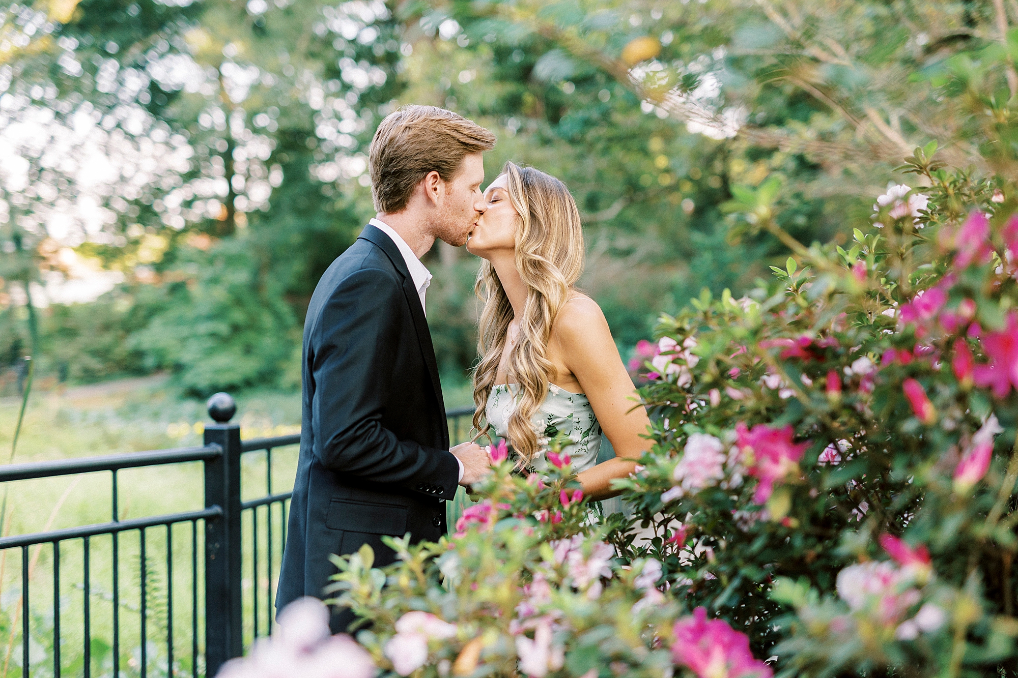 engaged couple kisses by bush of pink flowers in Rock Hill SC