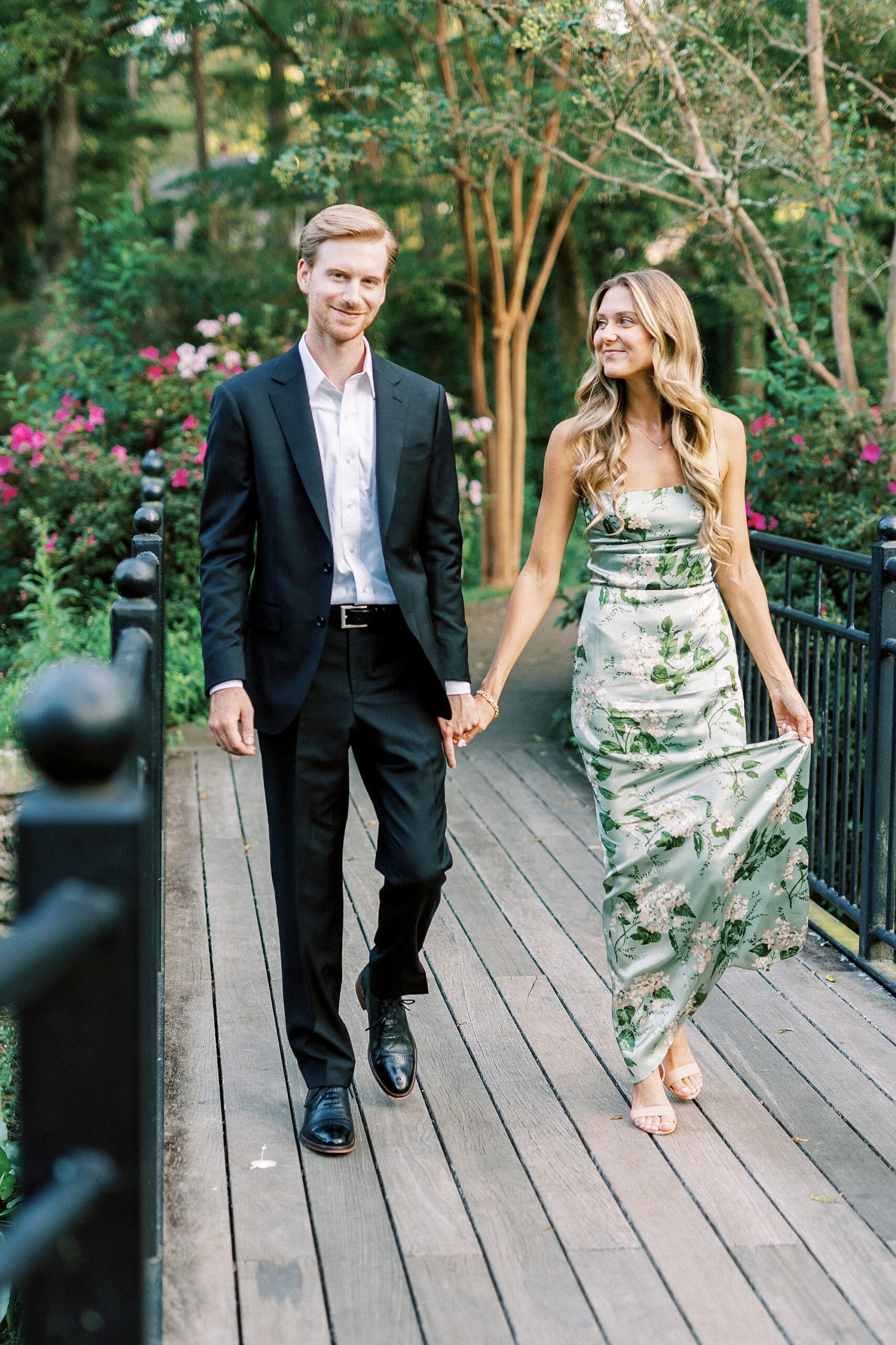 engaged couple holds hands walking on bridge inside Glencairn Garden