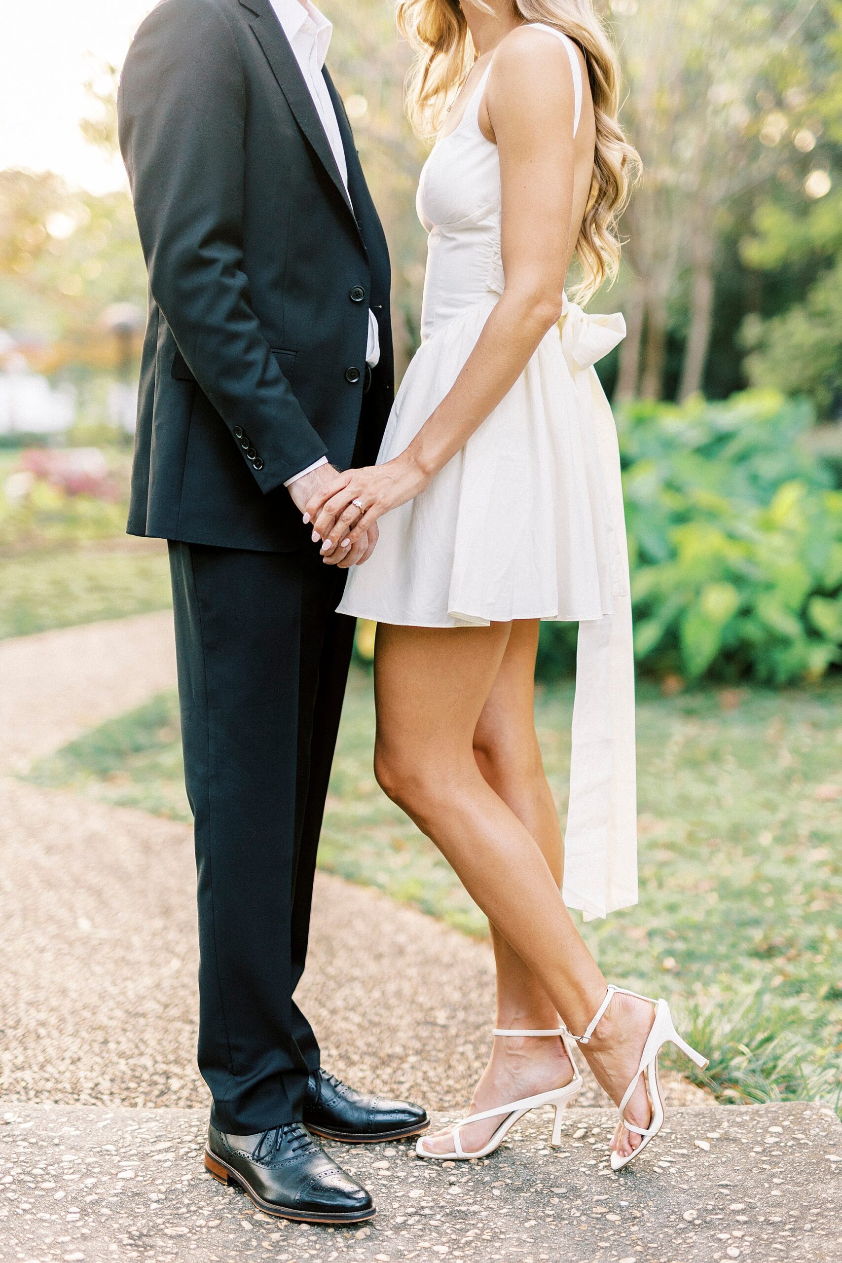 engaged couple holds hands showing off bride's shoes and white dress