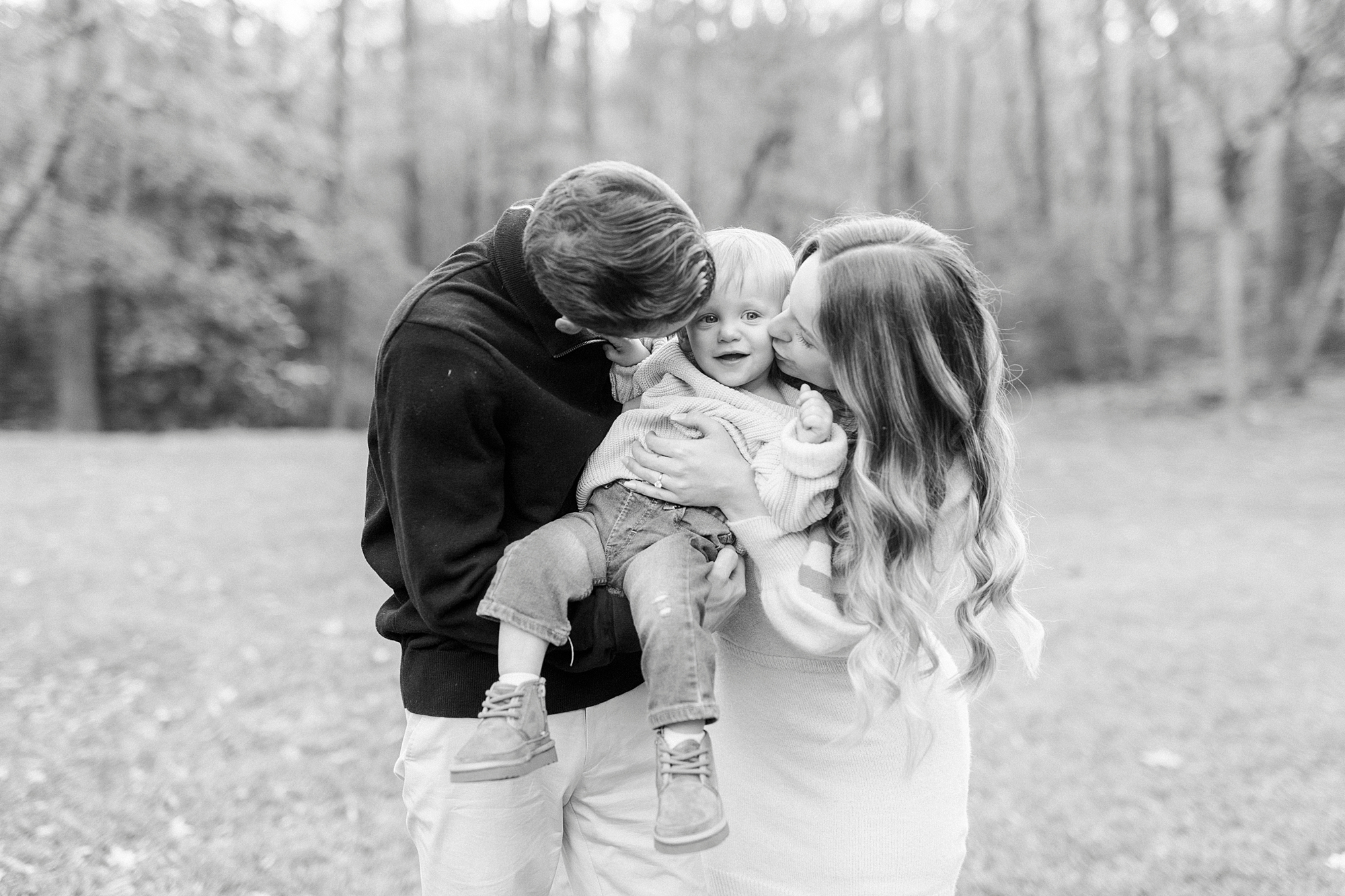 parents lean down to kiss son on cheeks hugging him tight during Baker's Creek Park family photos 