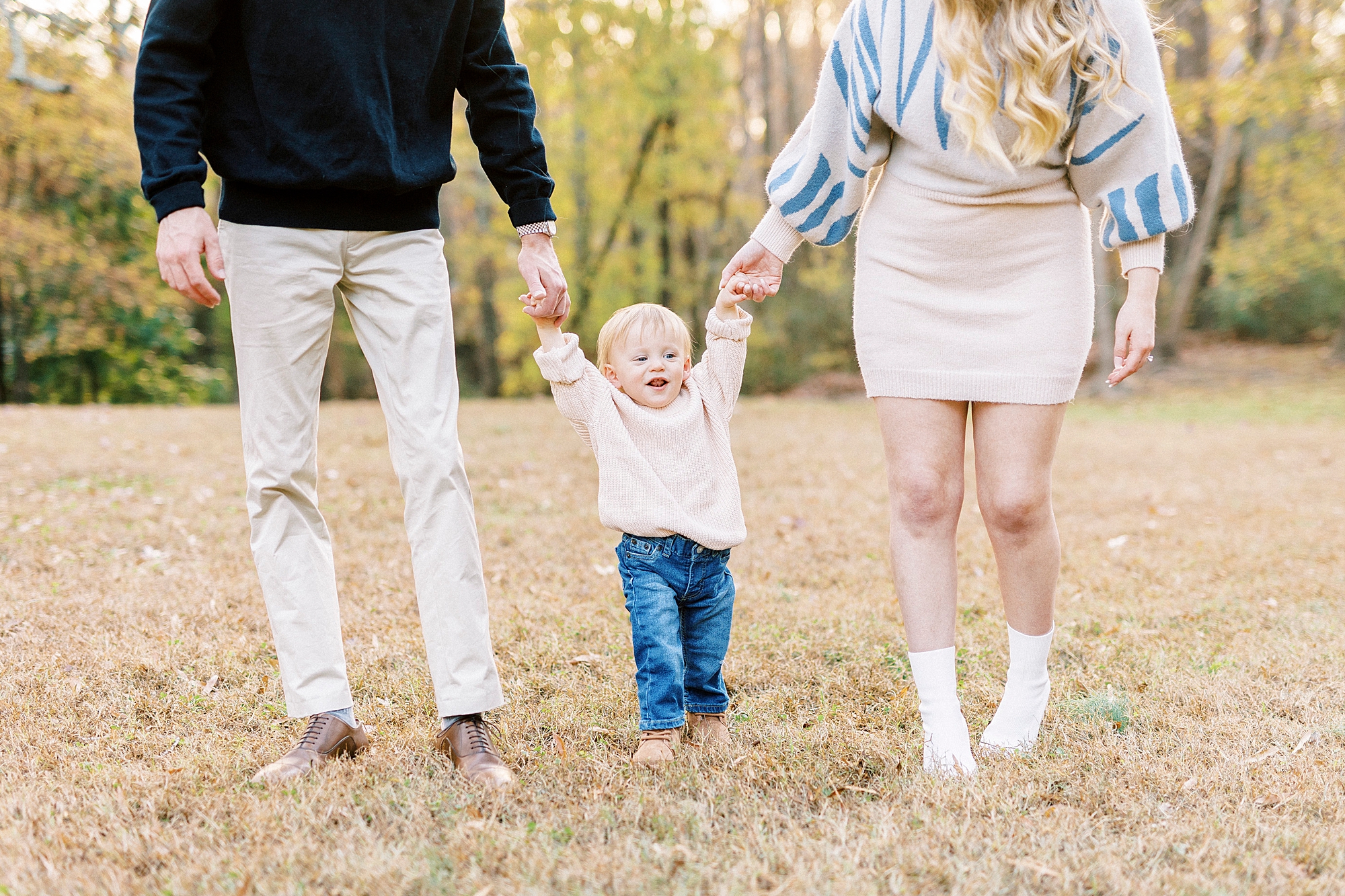 parents hold son's hand walking on dried grass during fall family photos 