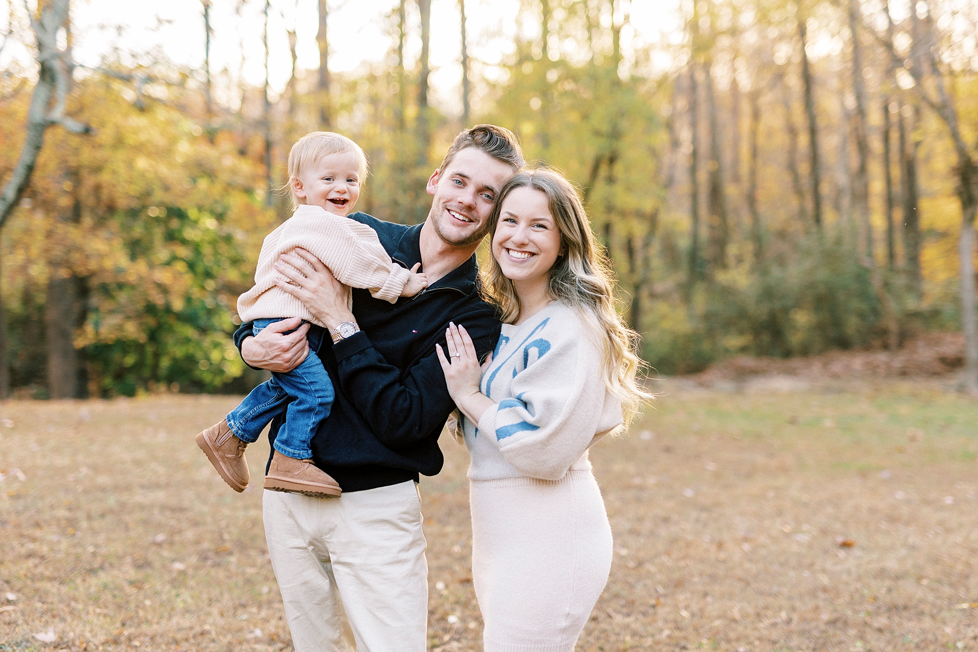 parents hug together with son laughing on dad's hip during fall family portraits at Baker's Creek Park