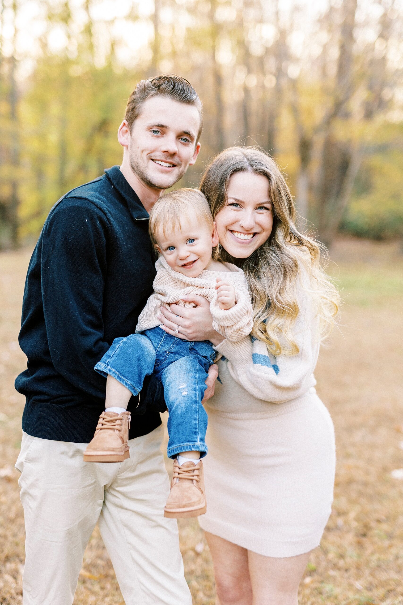 parents hug toddler son laughing during fall family photos 