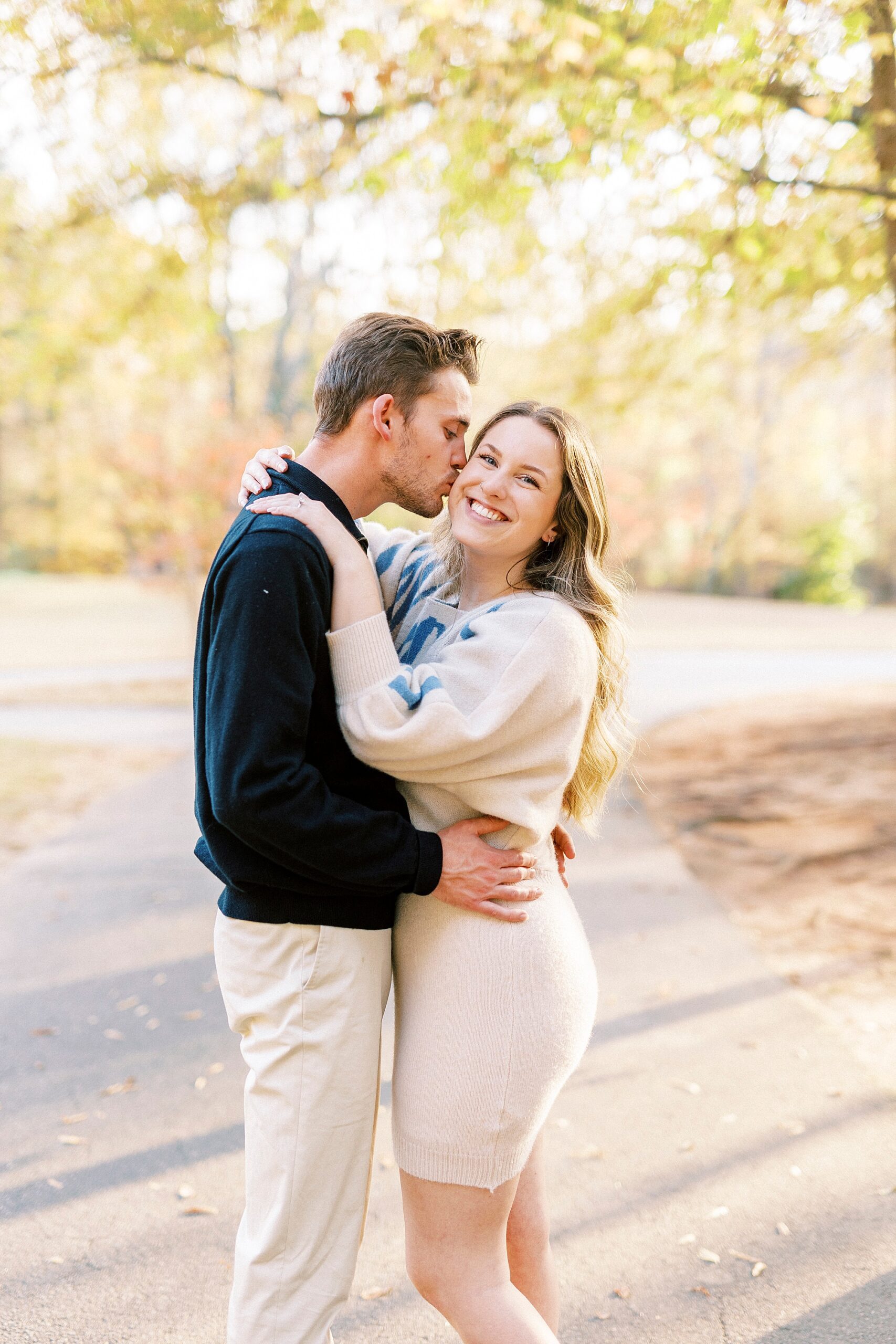 man hugs fiancee to him during Baker's Creek Park engagement session and kisses her cheek 