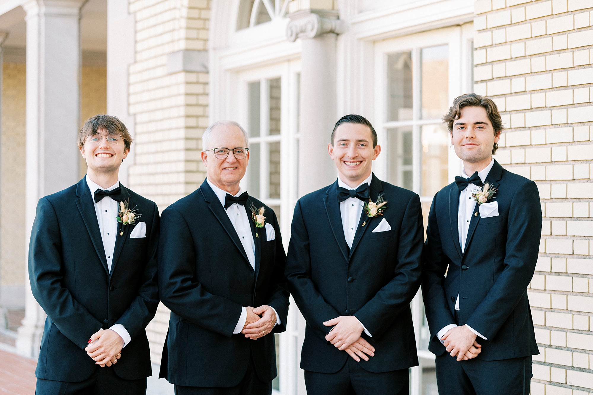 groom stands with groomsmen outside Separk Mansion with hands in front of them 