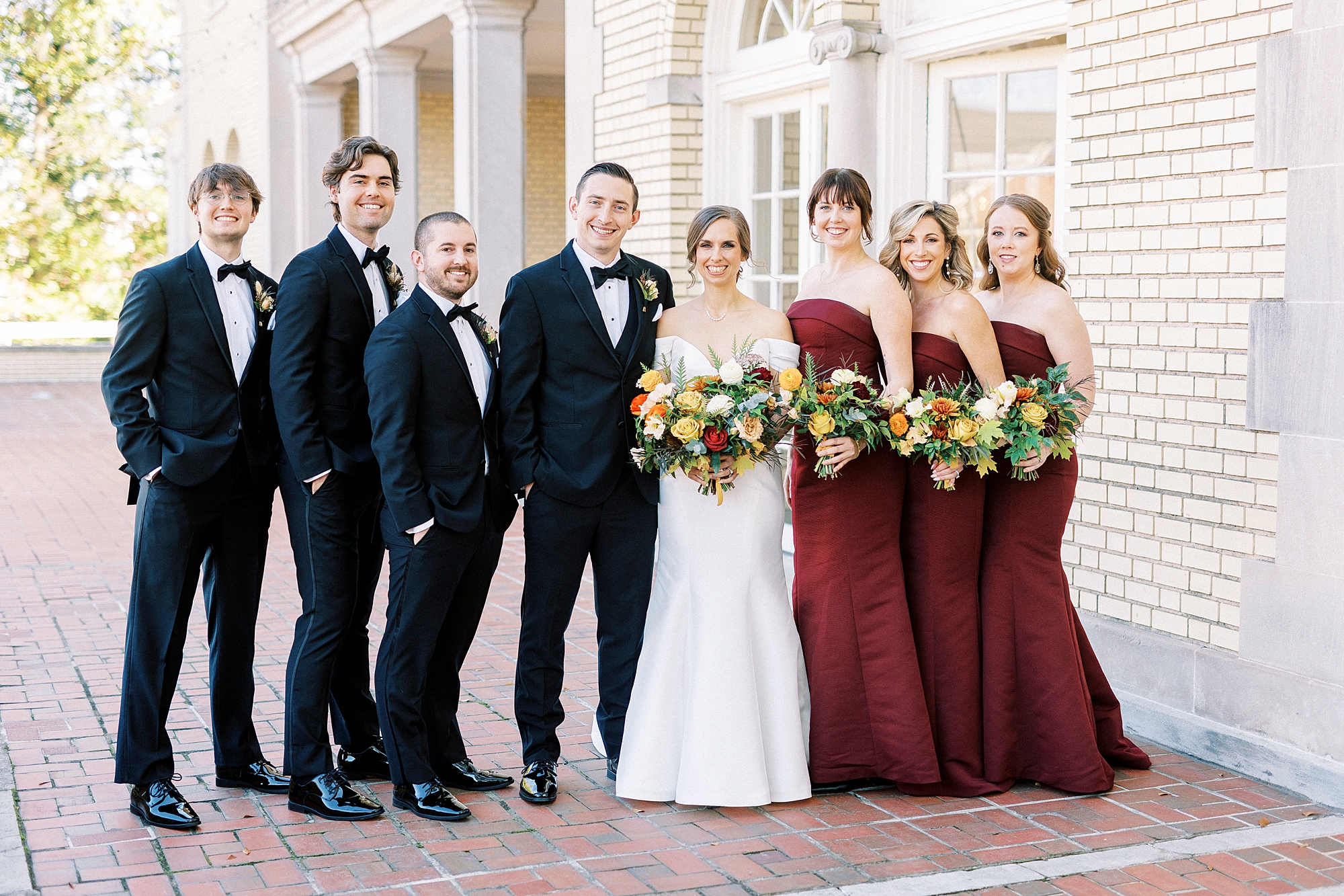 bride and groom pose with wedding party in red gown and black suits