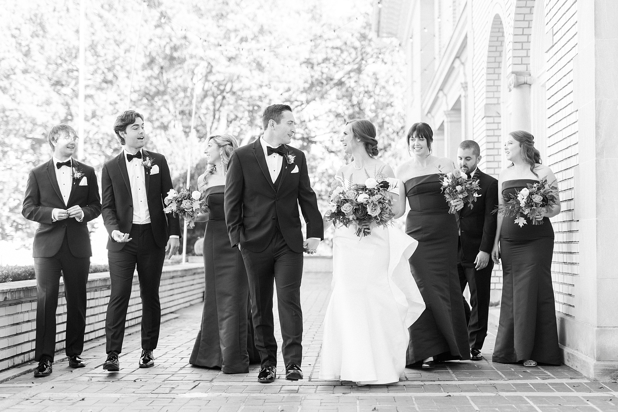 newlyweds hold hands walking with wedding party on patio at Separk Mansion