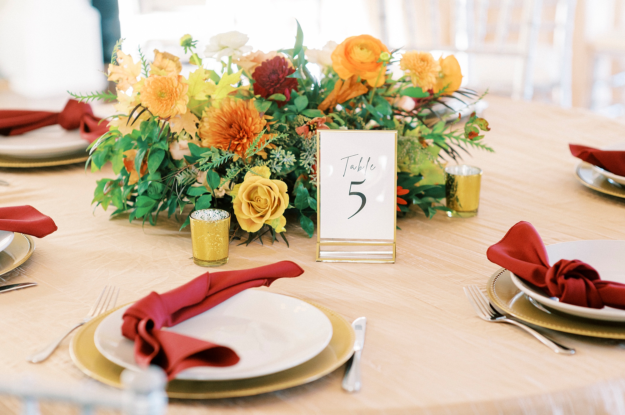 place setting with gold plates, burgundy napkins, and yellow and orange flowers