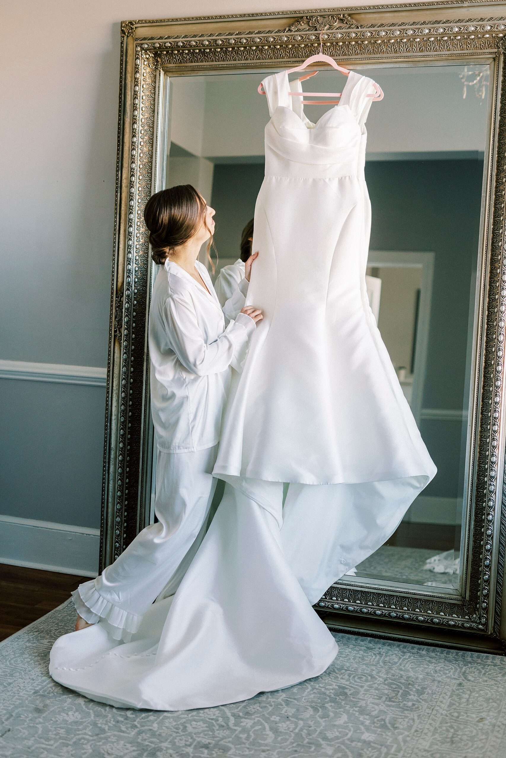 bride looks at wedding dress hanging on gold framed mirror inside Separk Mansion bridal suite 