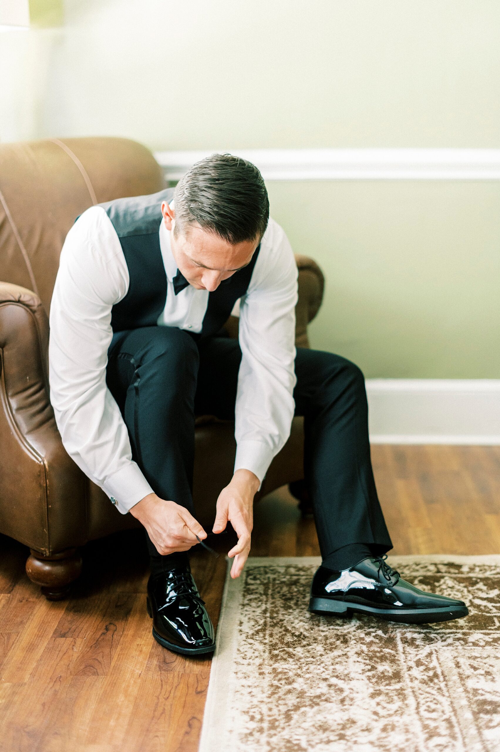groom sits in brown chair tying black shoes