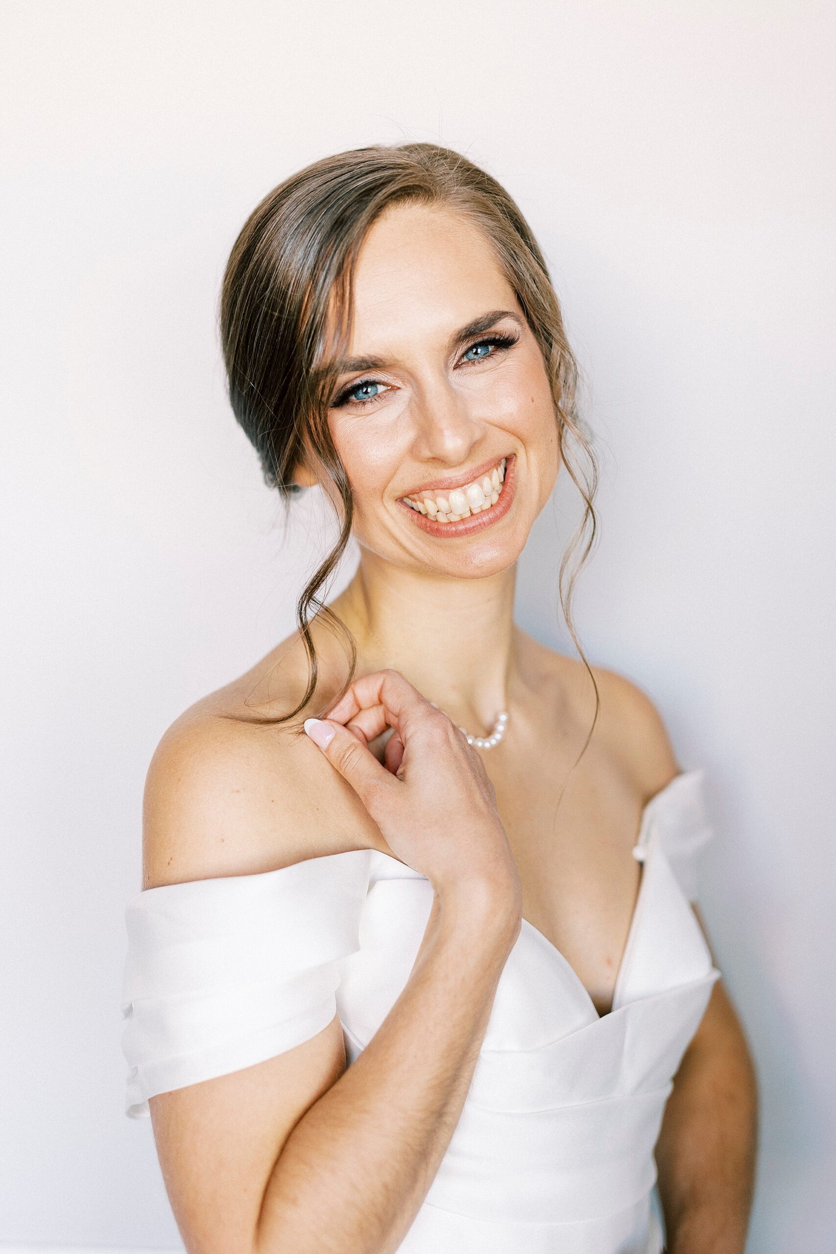 bride smiles in off-the-shoulder gown with pearl necklace 
