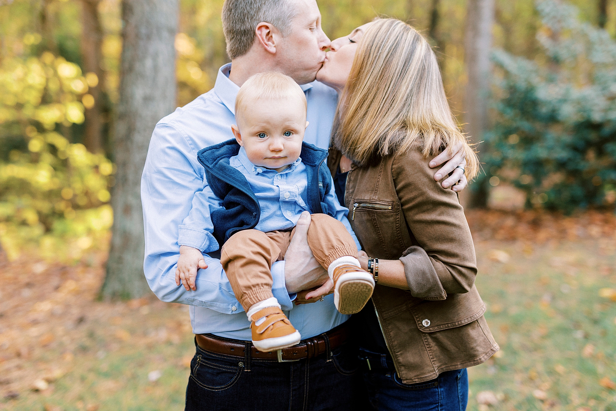 parents kiss while holding son between them during fall family portraits at Charlotte home