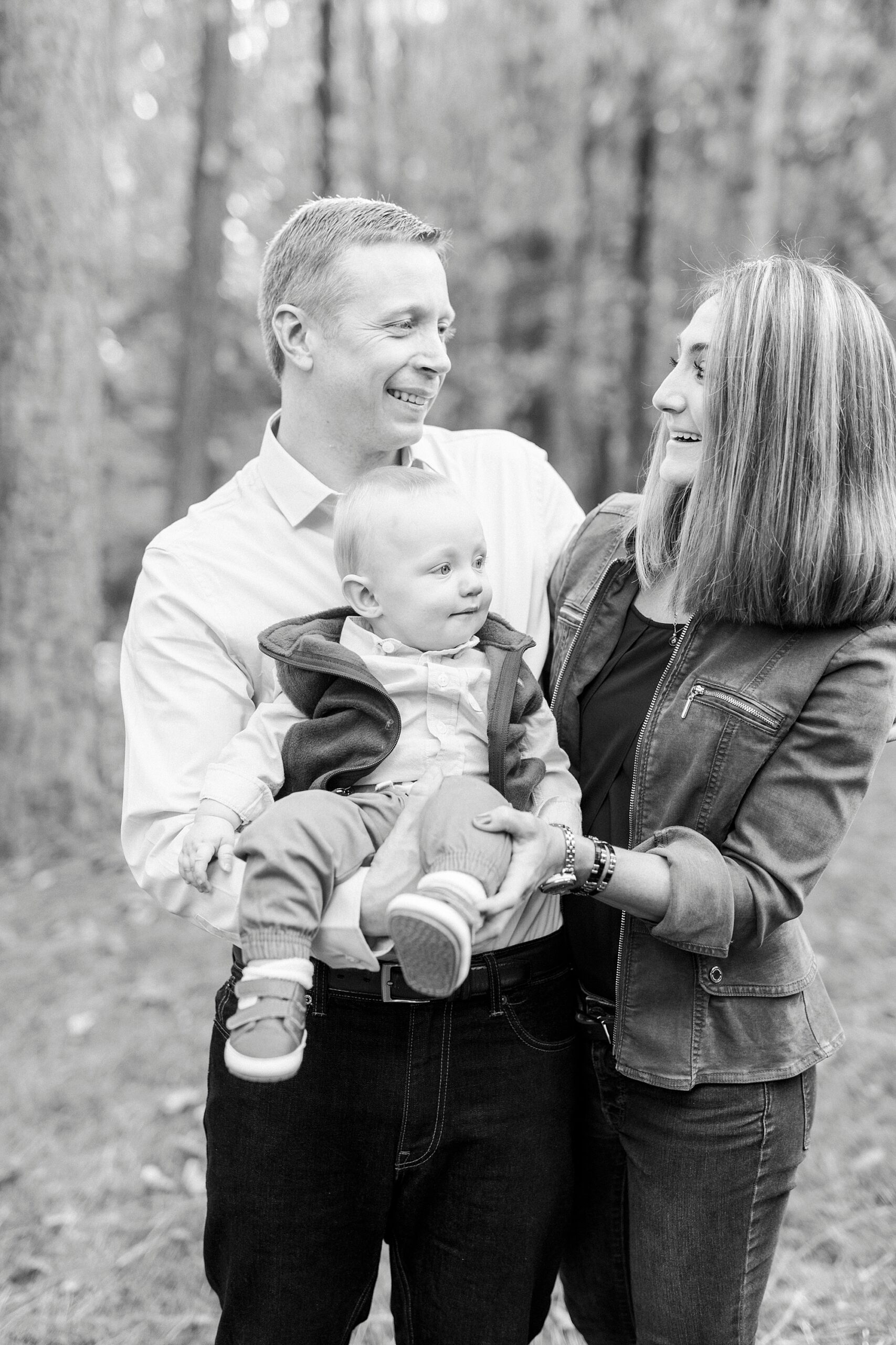 parents lean back smiling at each other while holding son during fall family portraits at Charlotte home