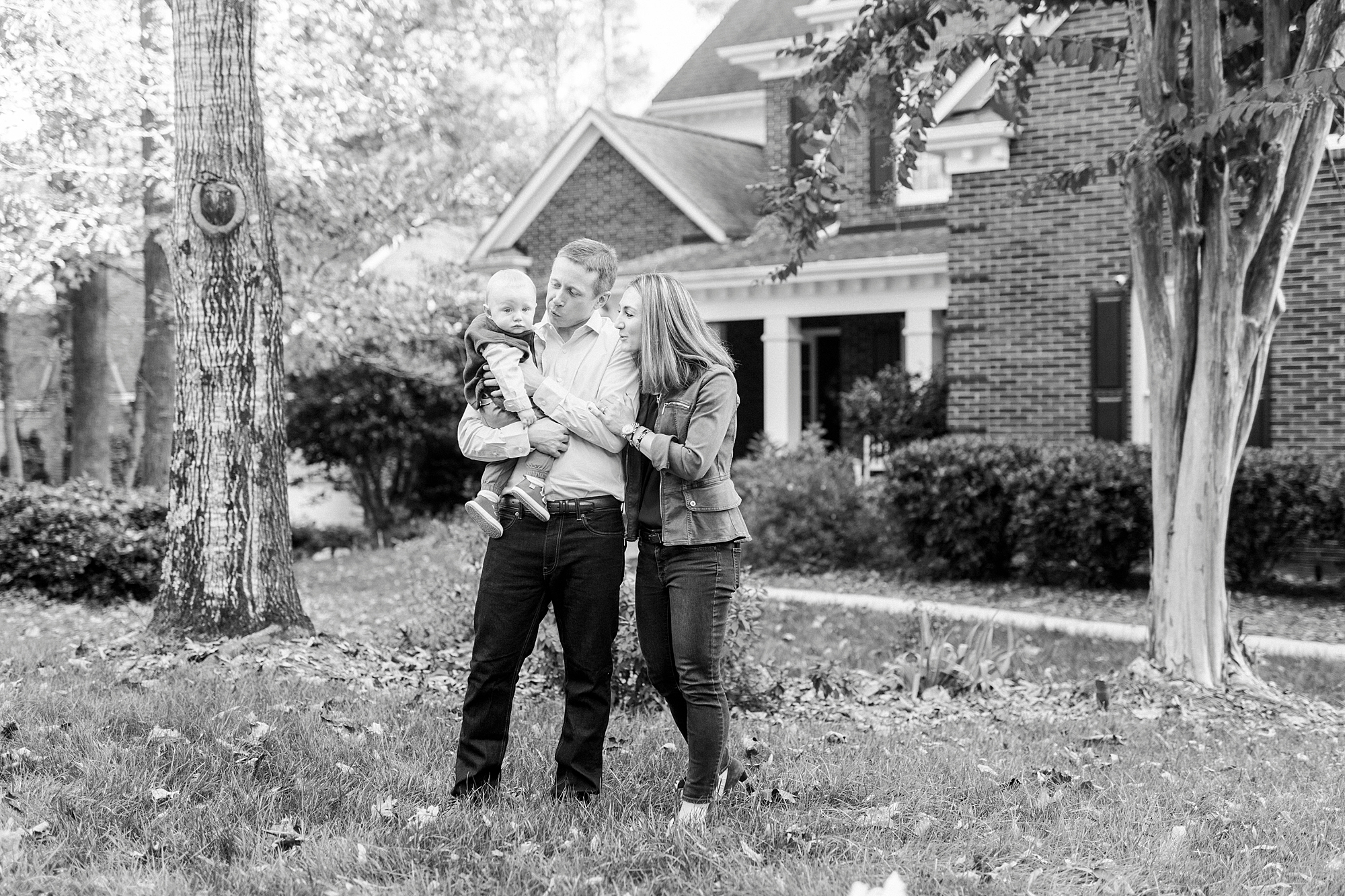mom looks over dad's shoulder at baby in his arms during fall family portraits at Charlotte home