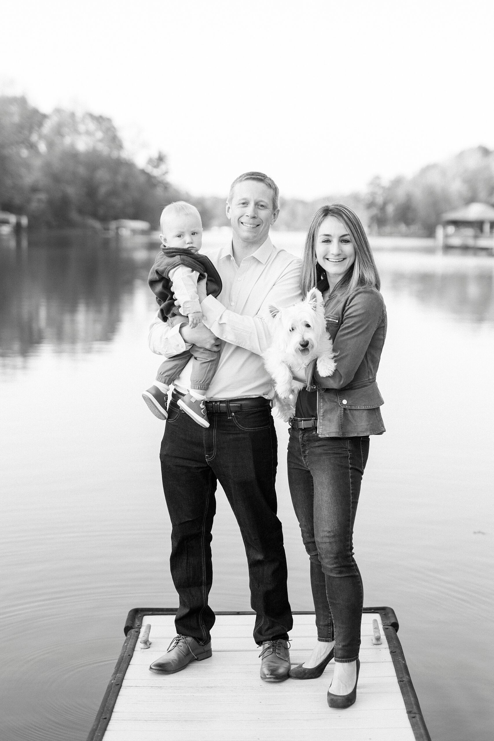 black and white photo of couple holding son on end of dock in Charlotte NC