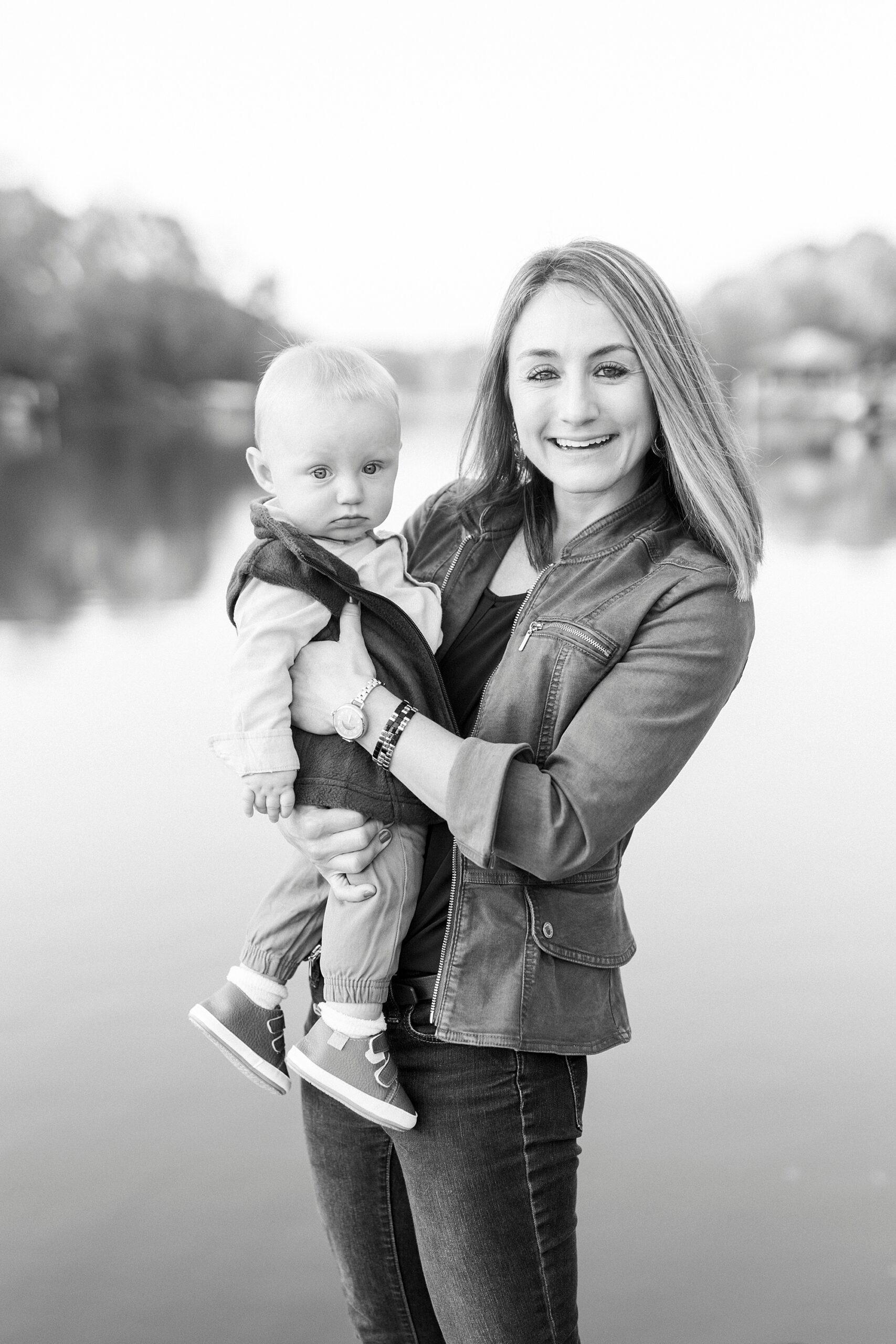 black and white photo of mom holding son on hip in front of lake during fall family portraits at Charlotte home