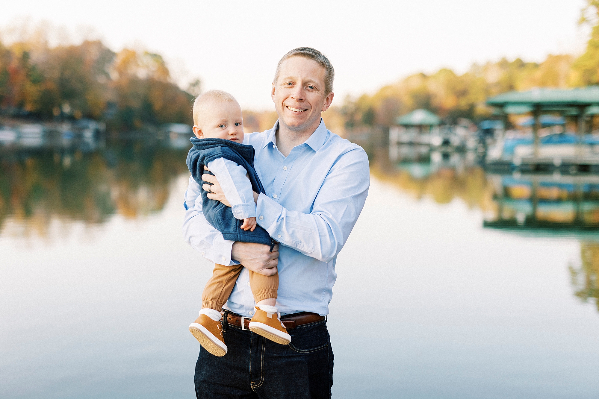 dad in blue button down shirt holds son on hip during fall family portraits at Charlotte home