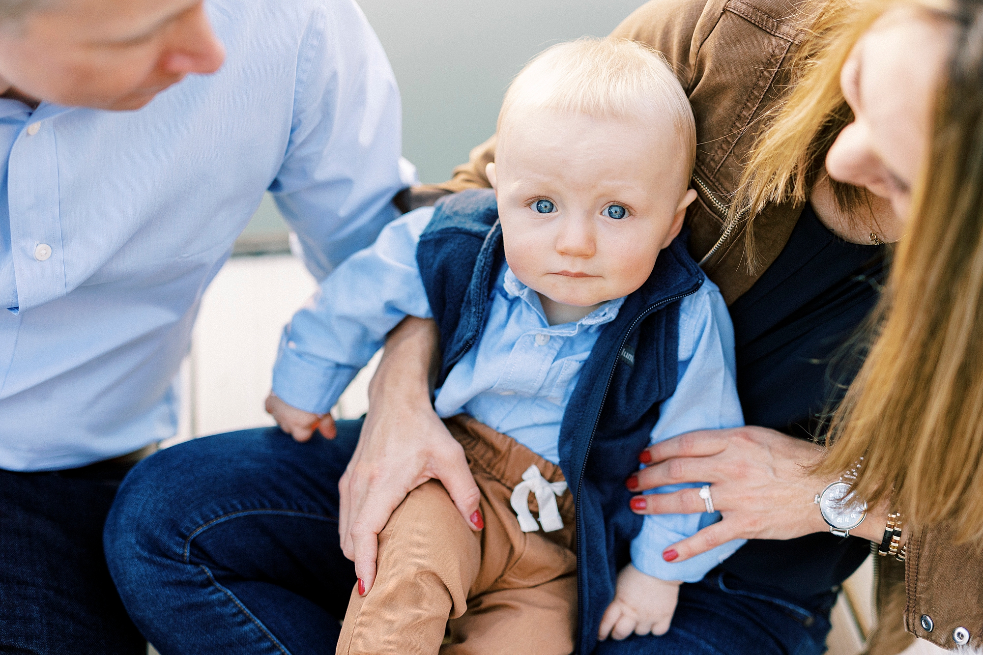 toddler sits on mom's lap in blue vest with brown pants