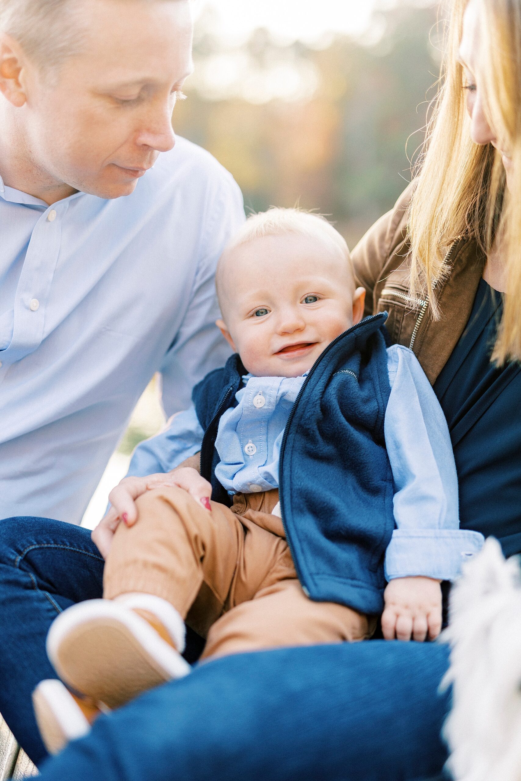 baby boy smiles leaning back in mom's arms during fall family portraits at Charlotte home