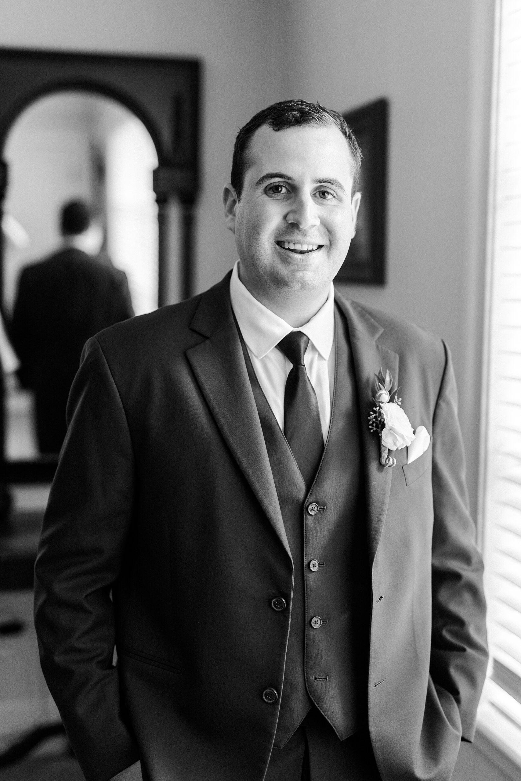 groom smiles standing with hands in pocket of suit 