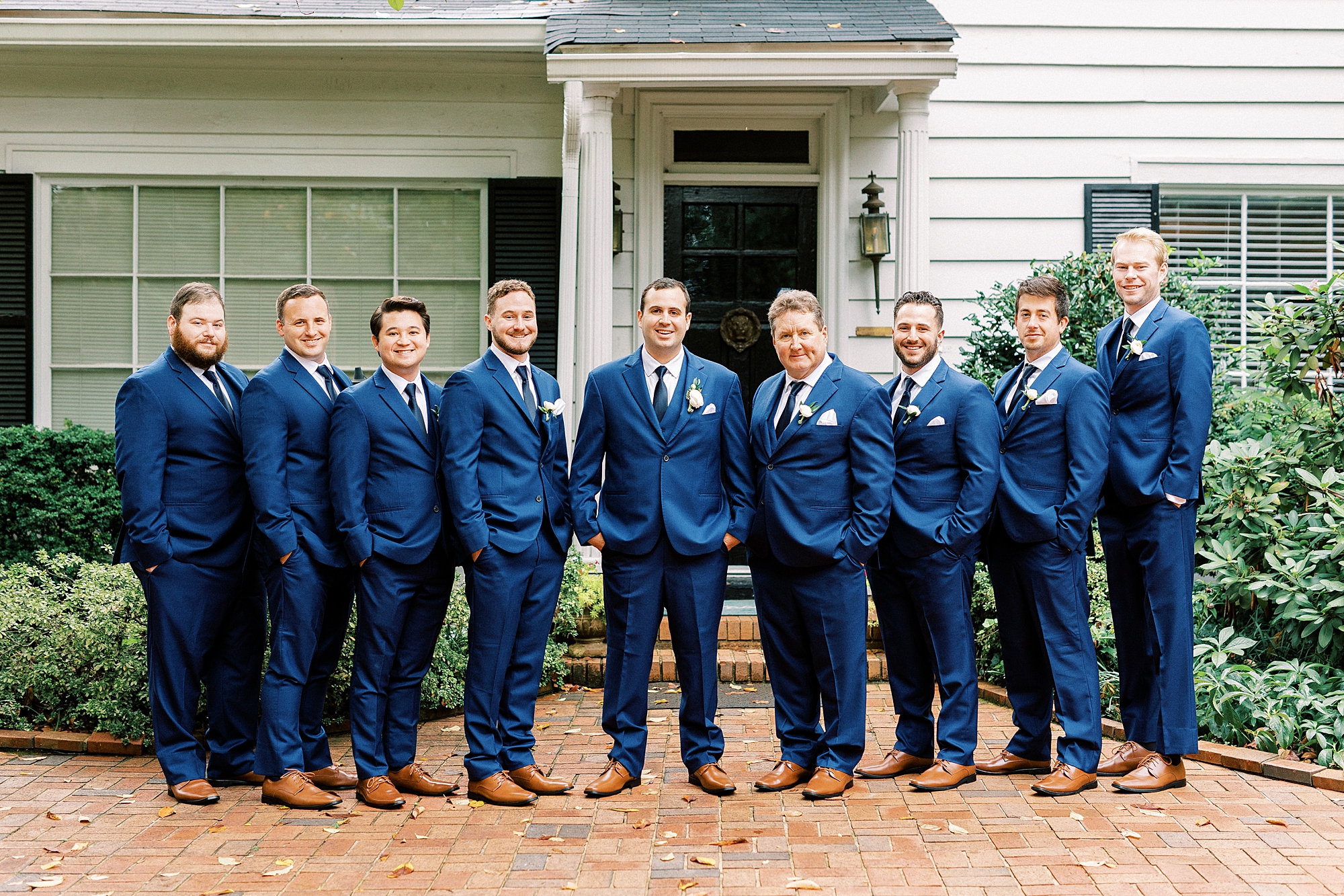 groom stands with groomsmen in blue suits outside the Morehead Inn