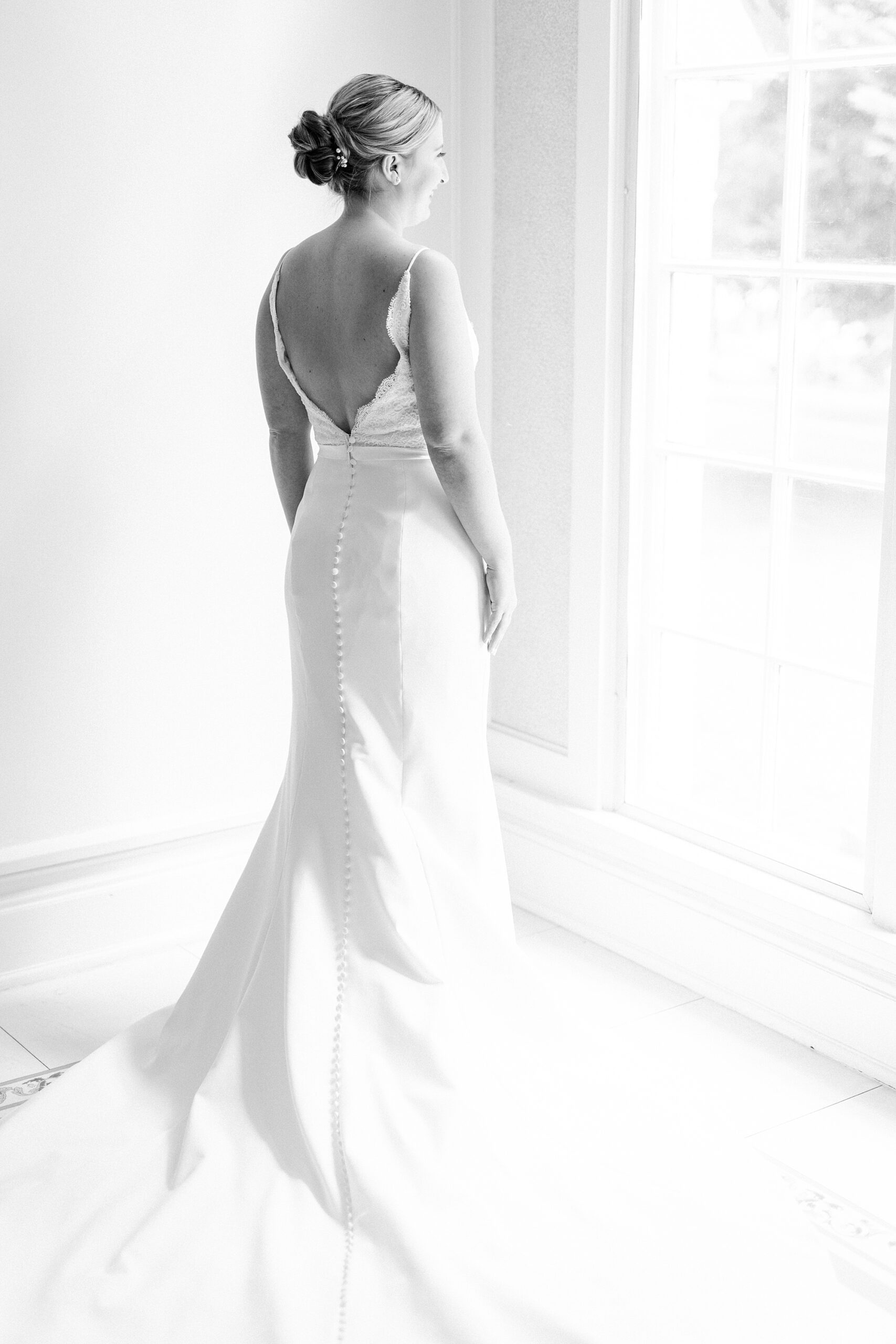 bride stands looking out window in wedding gown