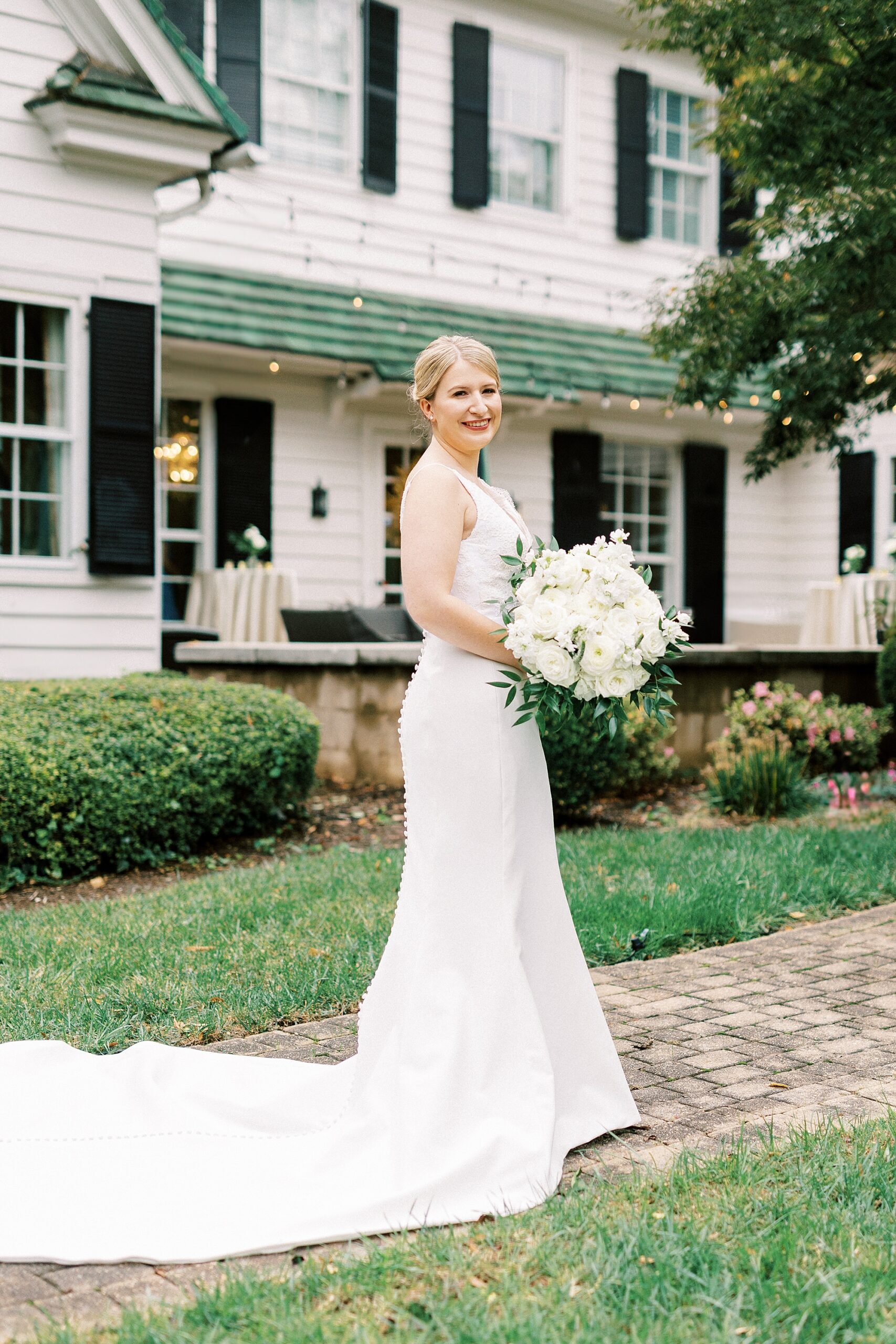 bride holds bouquet of ivory flowers in front of the Morehead Inn